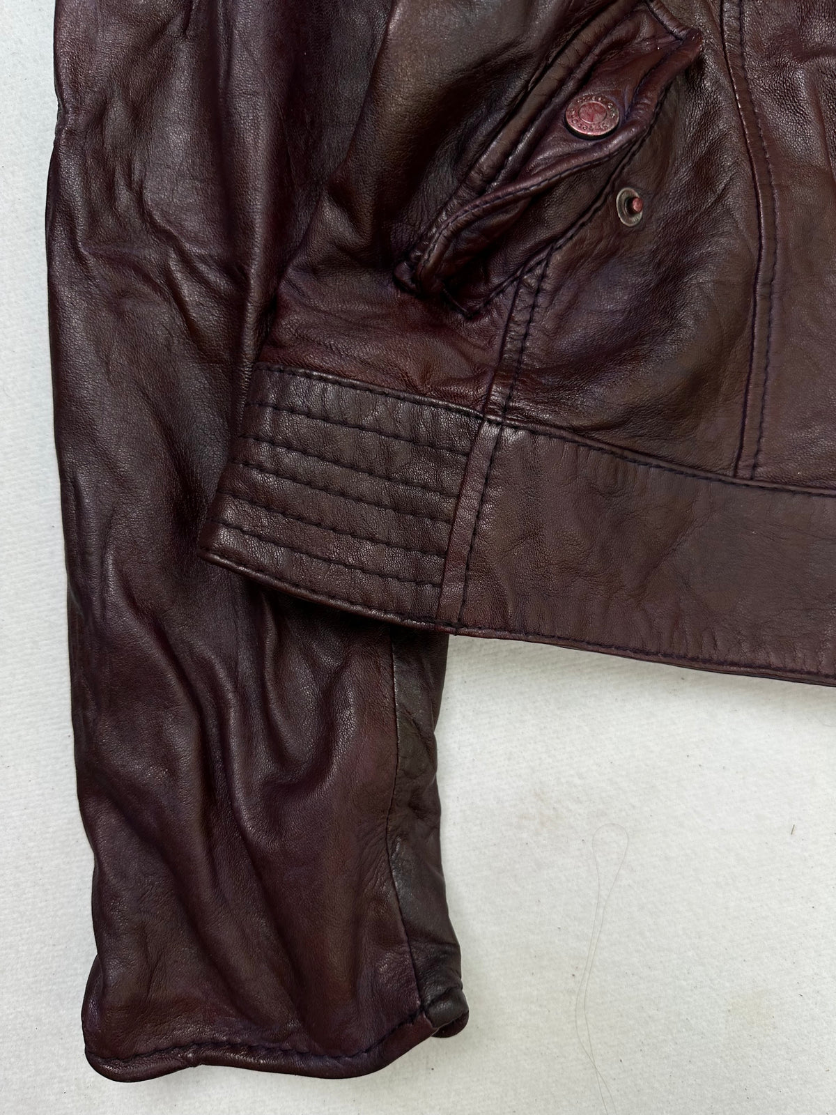 Close detail of the pockets and cuff on the size S burgundy leather biker jacket