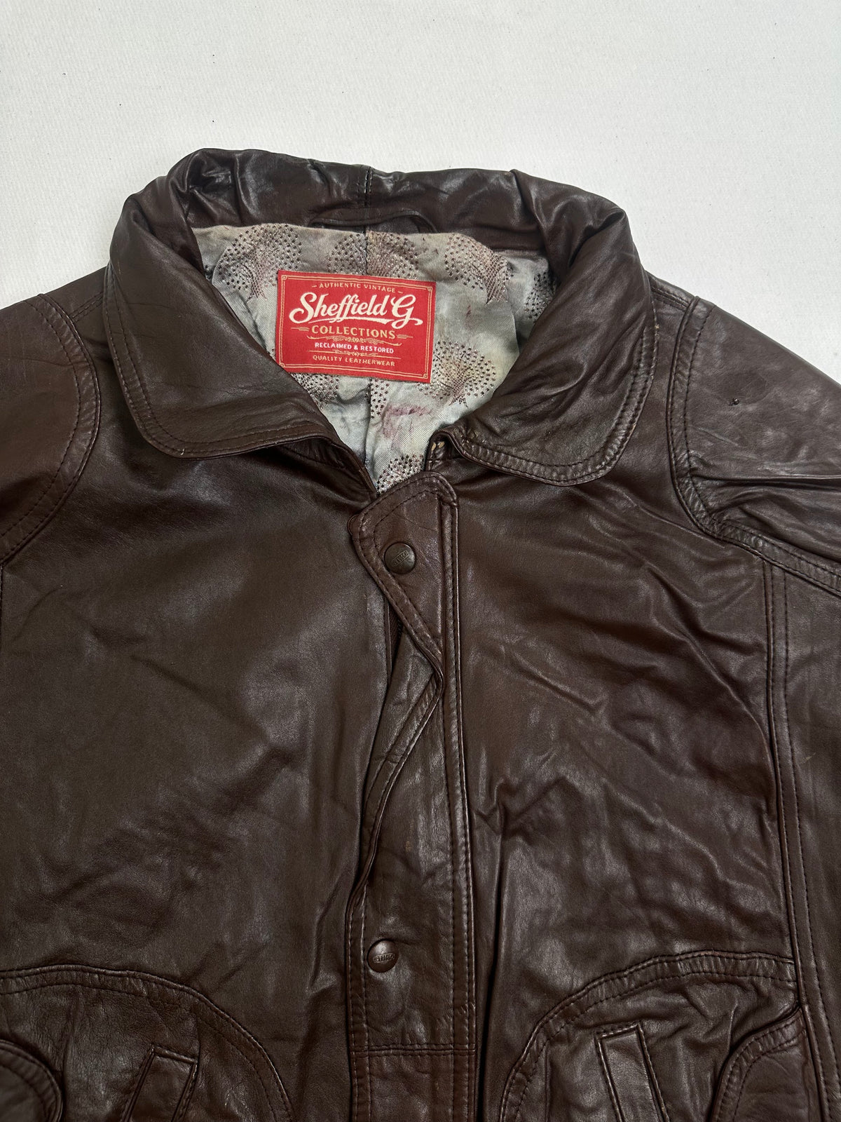 Rounded snap tab over a slanted welt pocket on the brown jacket