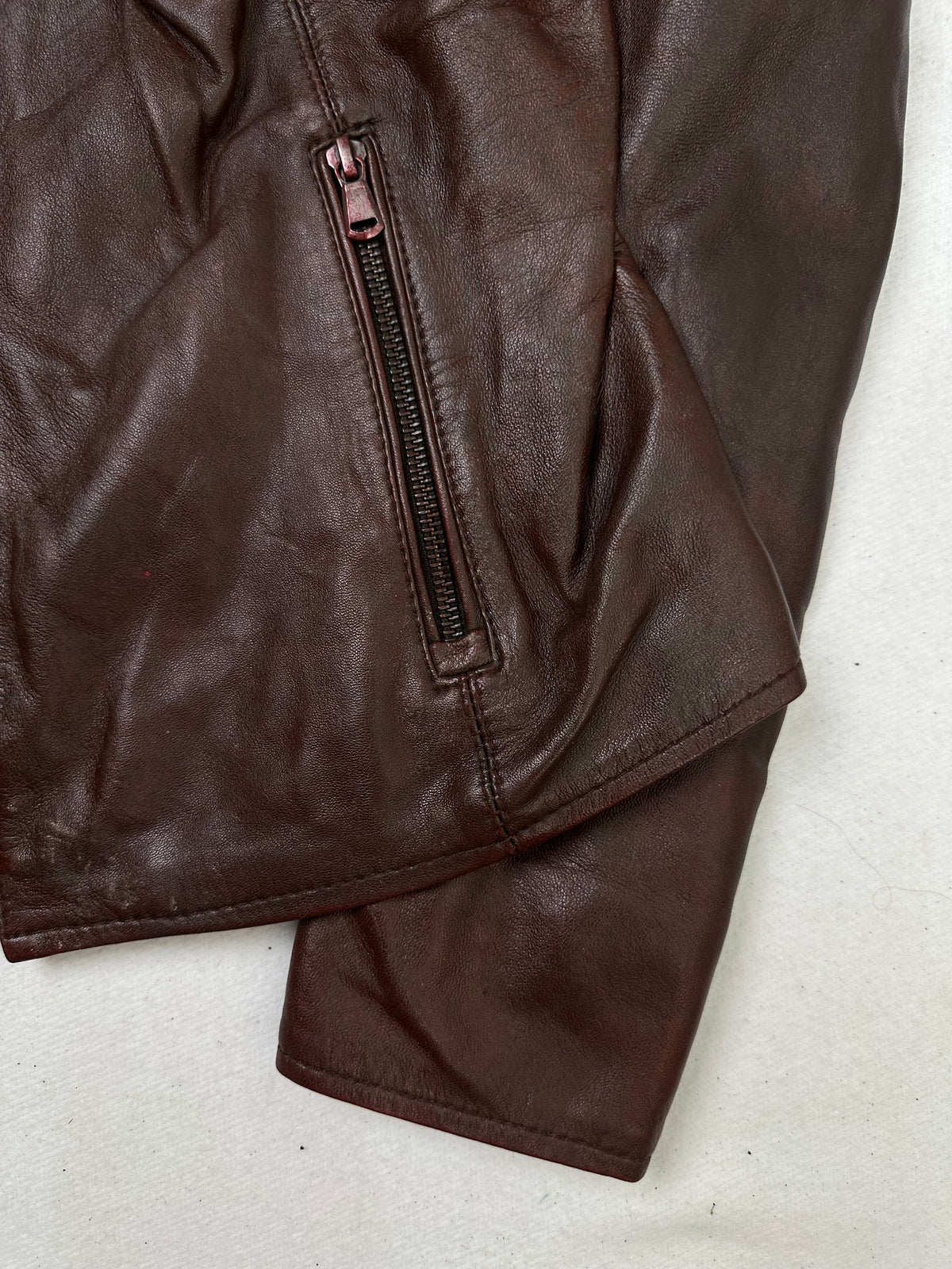 Side pocket and hem of the size XS burgundy leather cafe racer jacket, up close