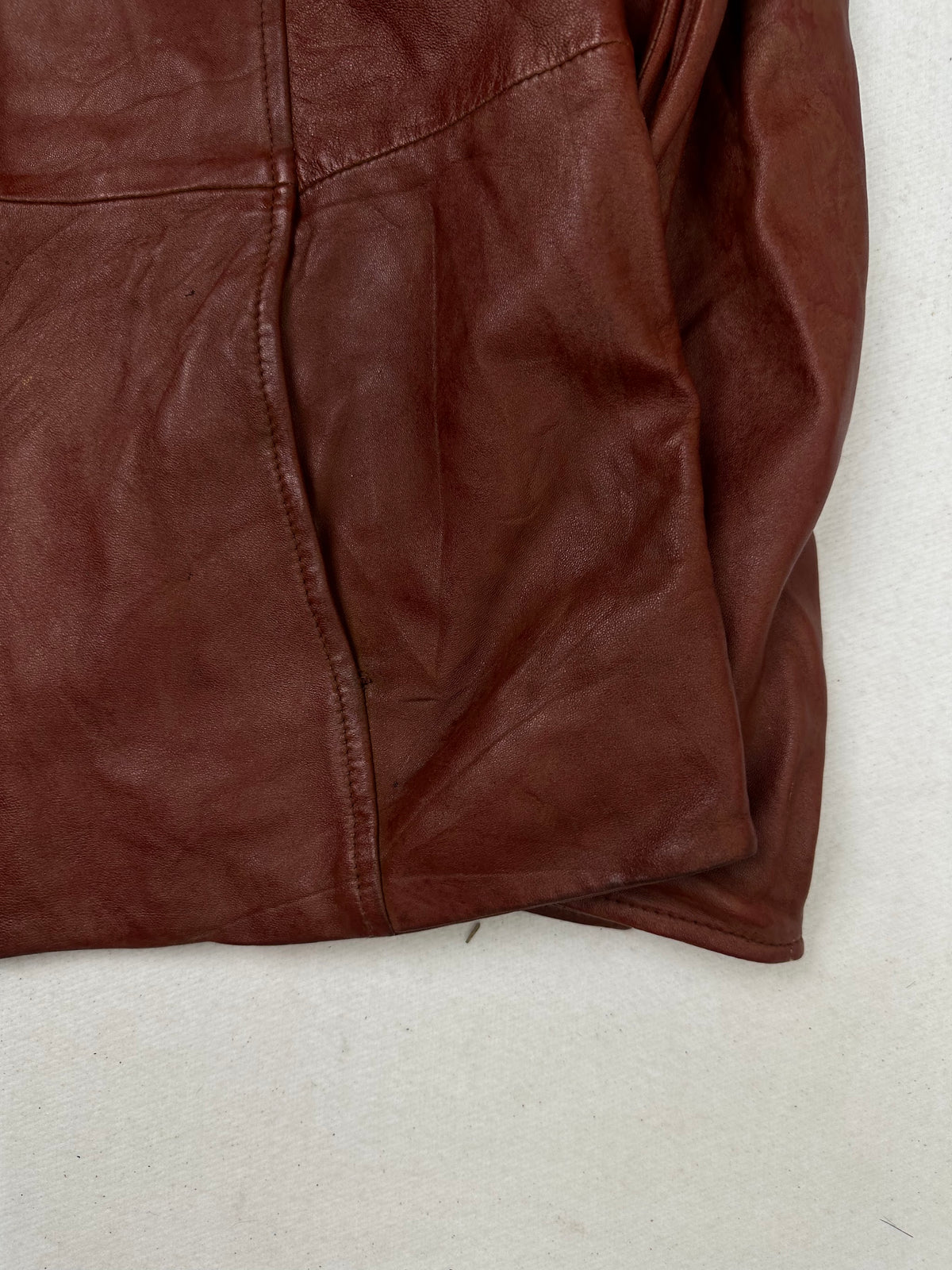 Side pocket and hem of the size S burgundy leather cafe racer jacket, up close