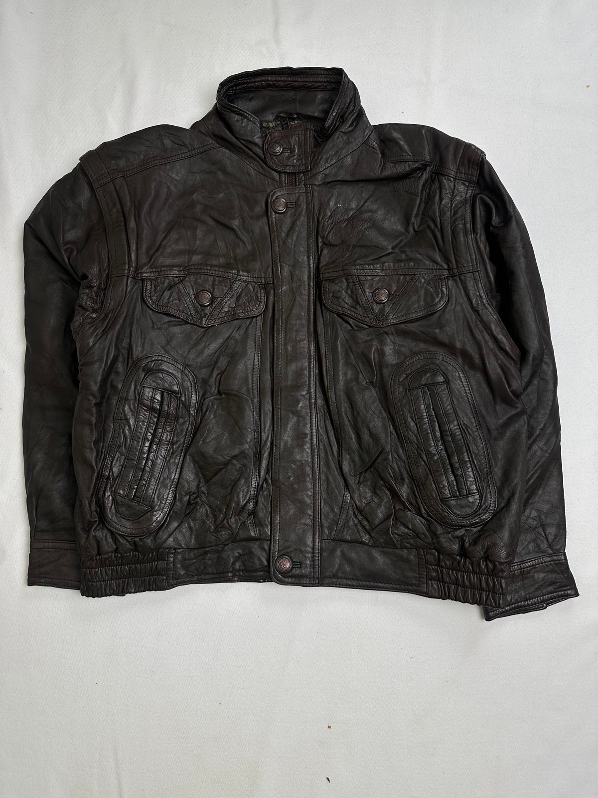 Front of the brown leather flight jacket showing the twin snap-flap chest pockets above the oval padded panels