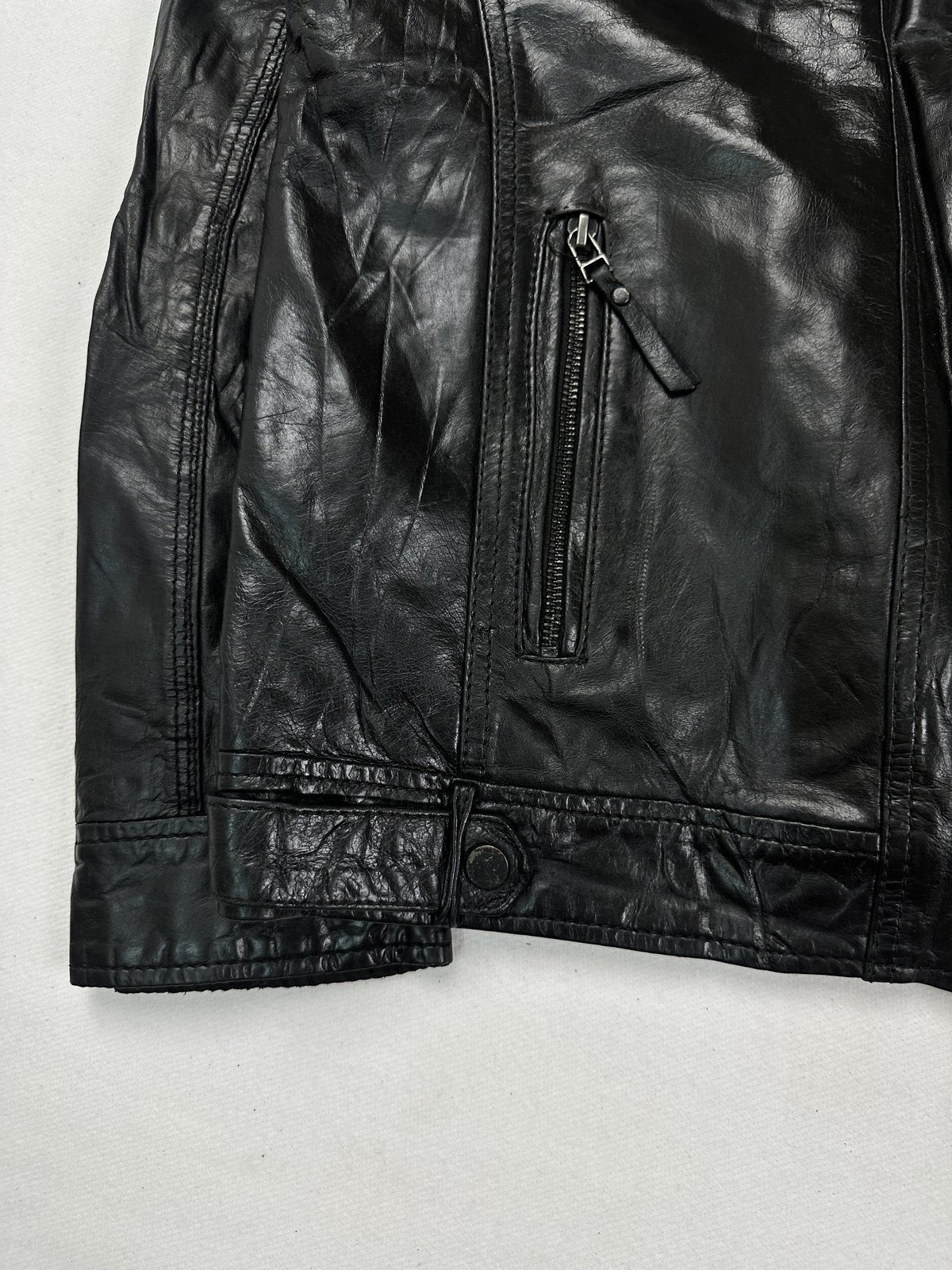 Lower front zip pocket and the snap tab at the hem of the black leather jacket