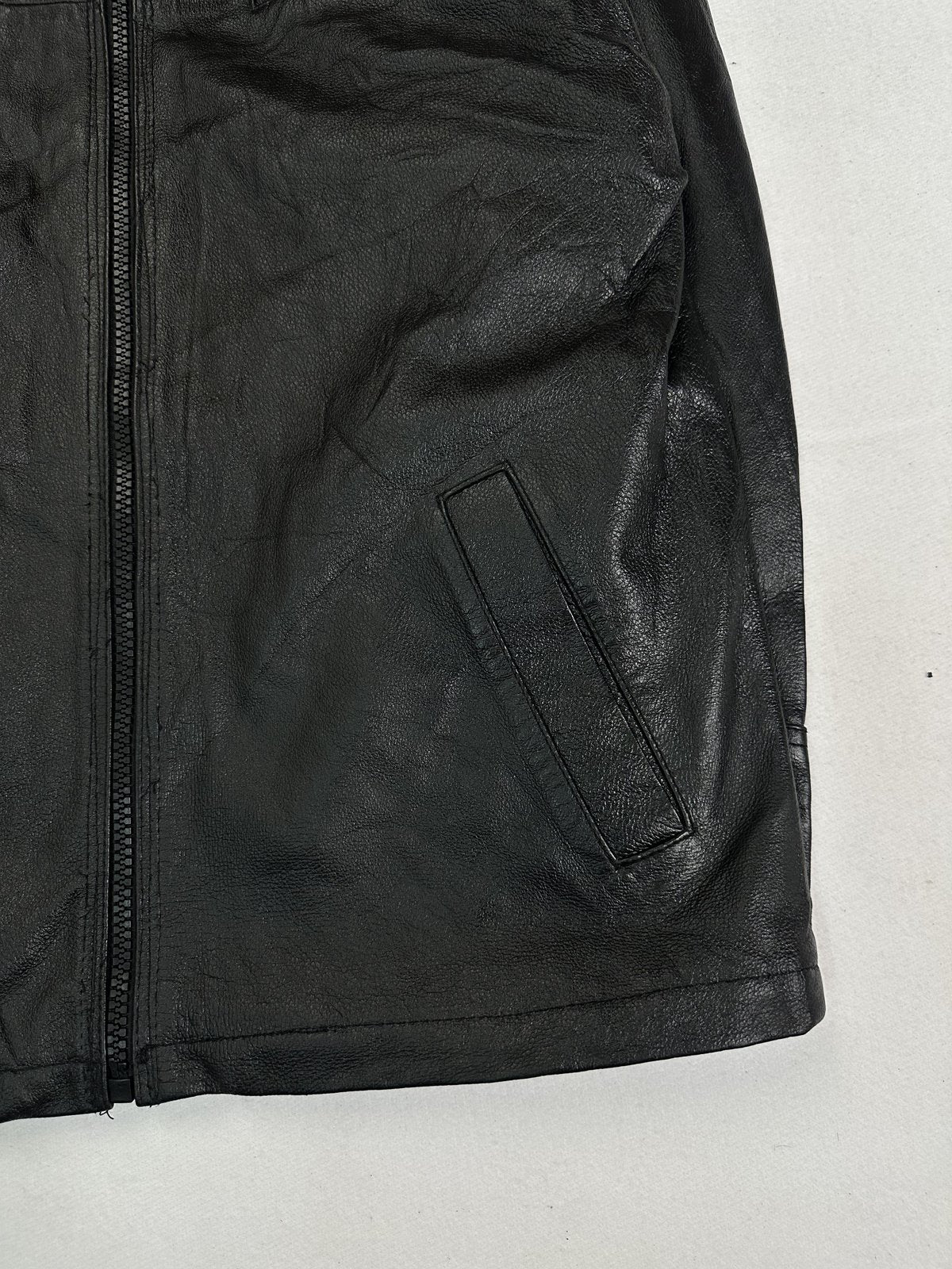 Angled detail of the front zip beside a slanted welt pocket on the black leather