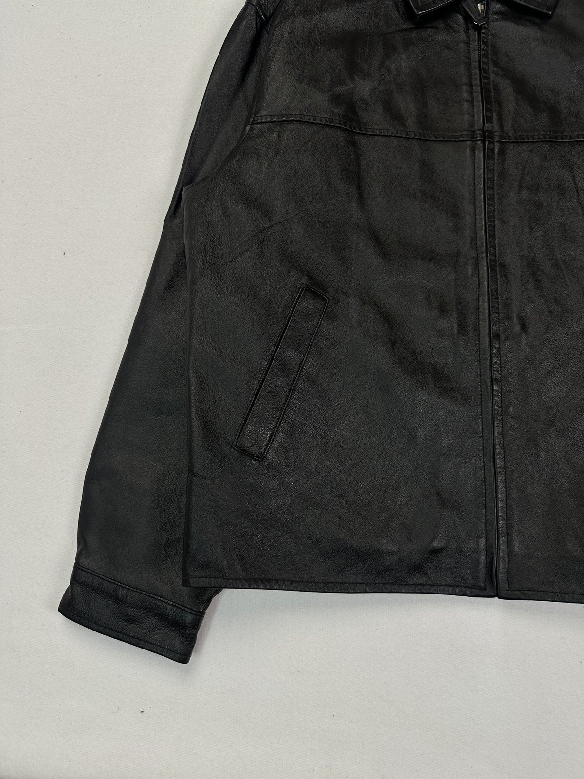 Lower left front of the black leather jacket with a slanted welt pocket and straight hem