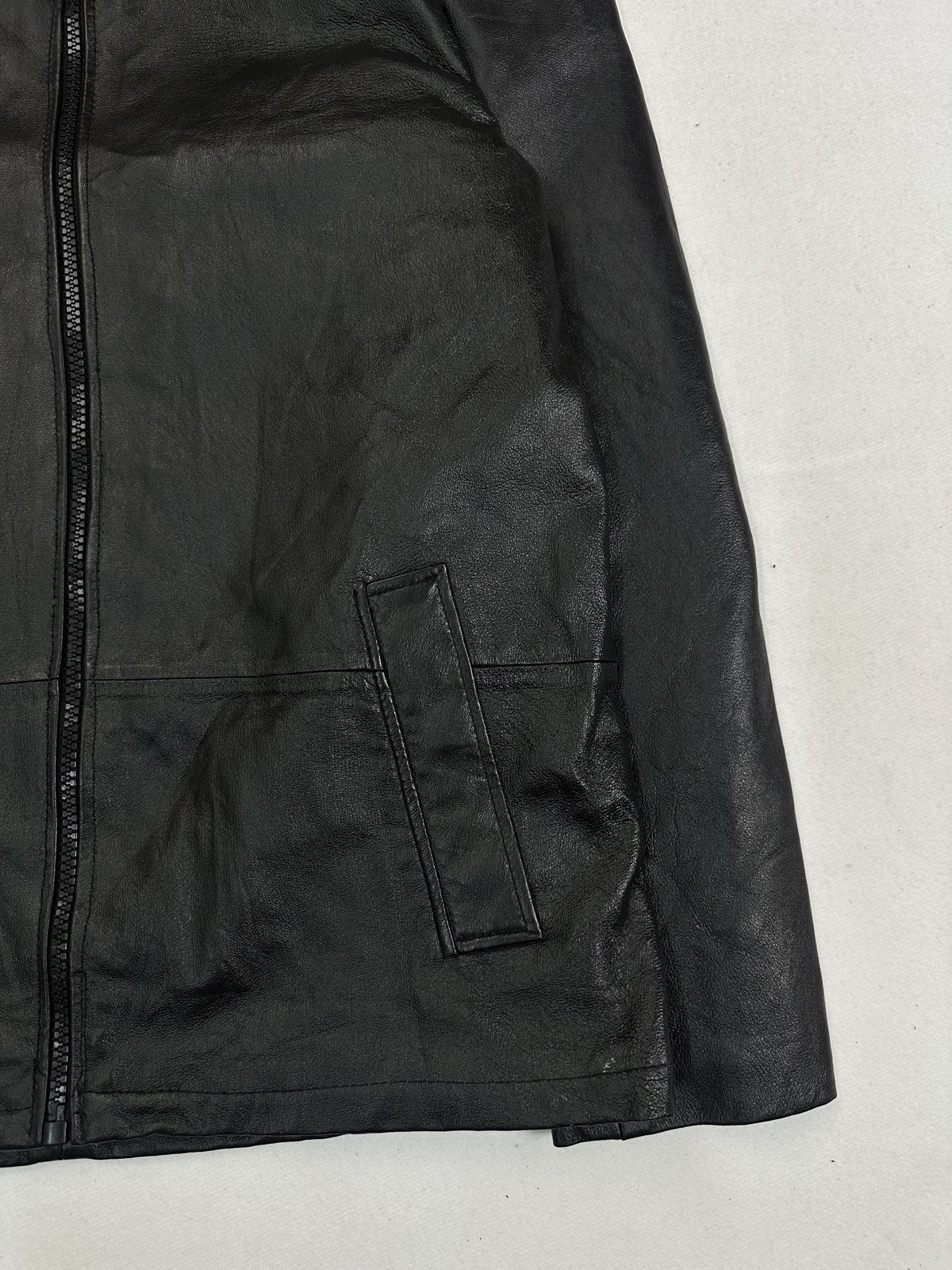 Angled view of a slanted welt pocket and the front zip on the black leather
