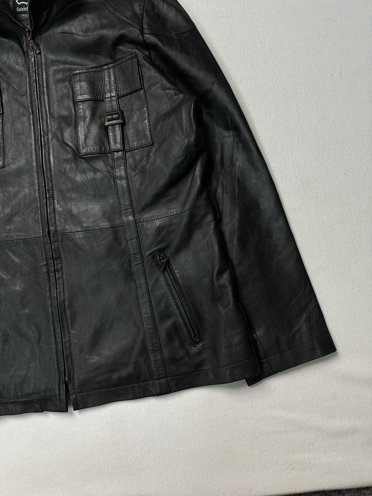 Angled view of the right hand zip pocket and the long straight hem on the black leather