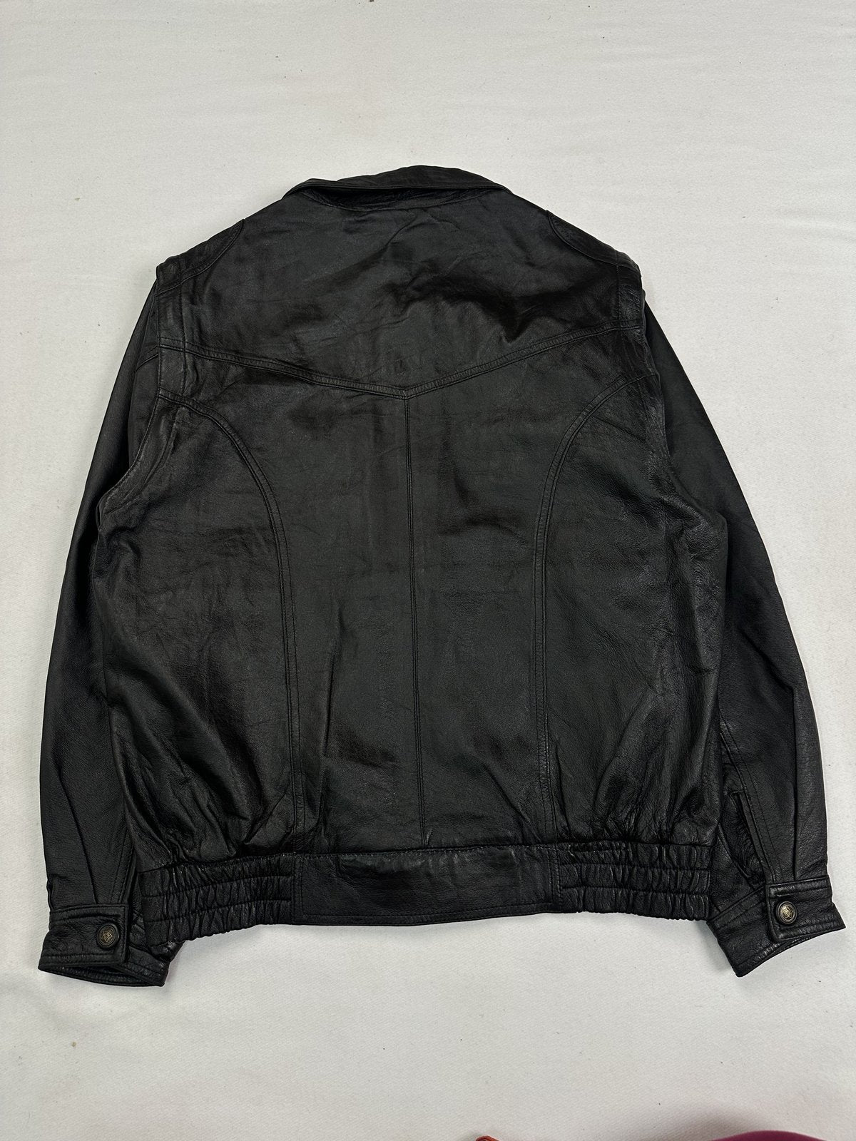 Rear view of the black bomber laid flat, showing the yoke seam and elasticated waist
