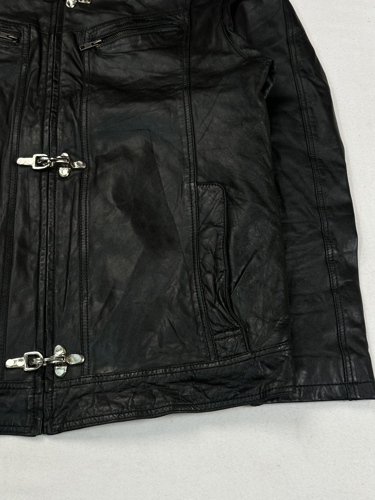 Angled view of a chest zip pocket and the row of hook clasps on the black leather