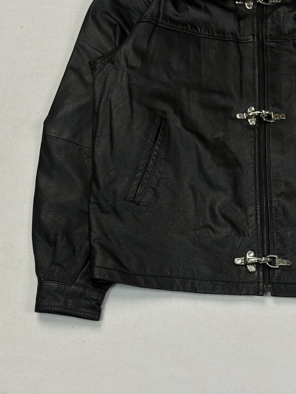 Lower front corner showing a welt hand pocket and the turned-back cuff on black leather