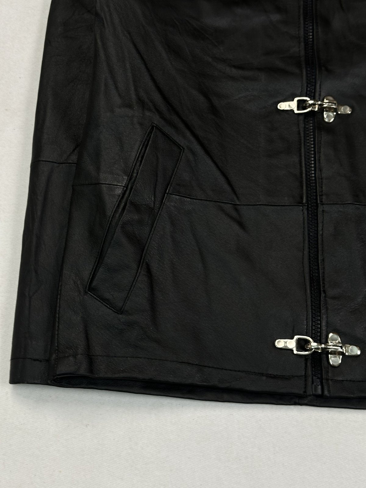 Lower left front with an angled slash pocket and two silver hook clasps beside the zip