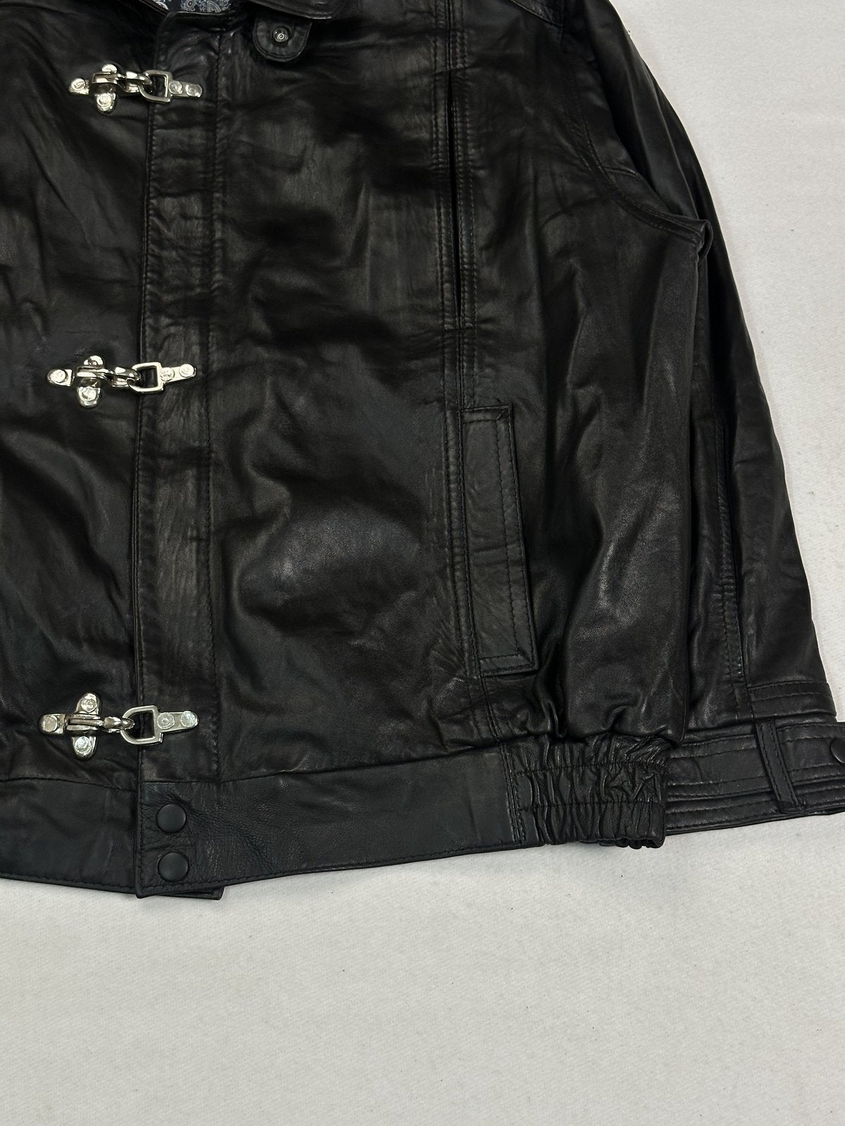 Angled view of the clasp fastenings and a slanted welt pocket on the black leather