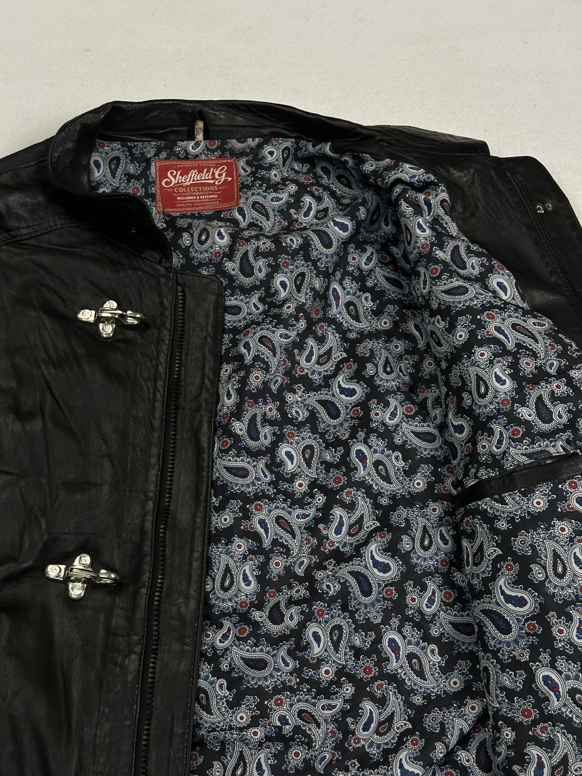 Grey and blue paisley lining inside the black jacket, seen close up at the shoulder