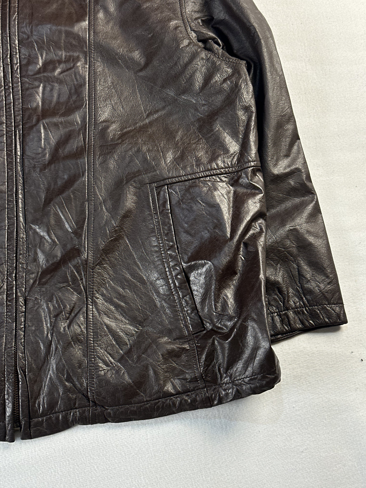 Slash pocket and hem at the right side of the glossy brown leather jacket
