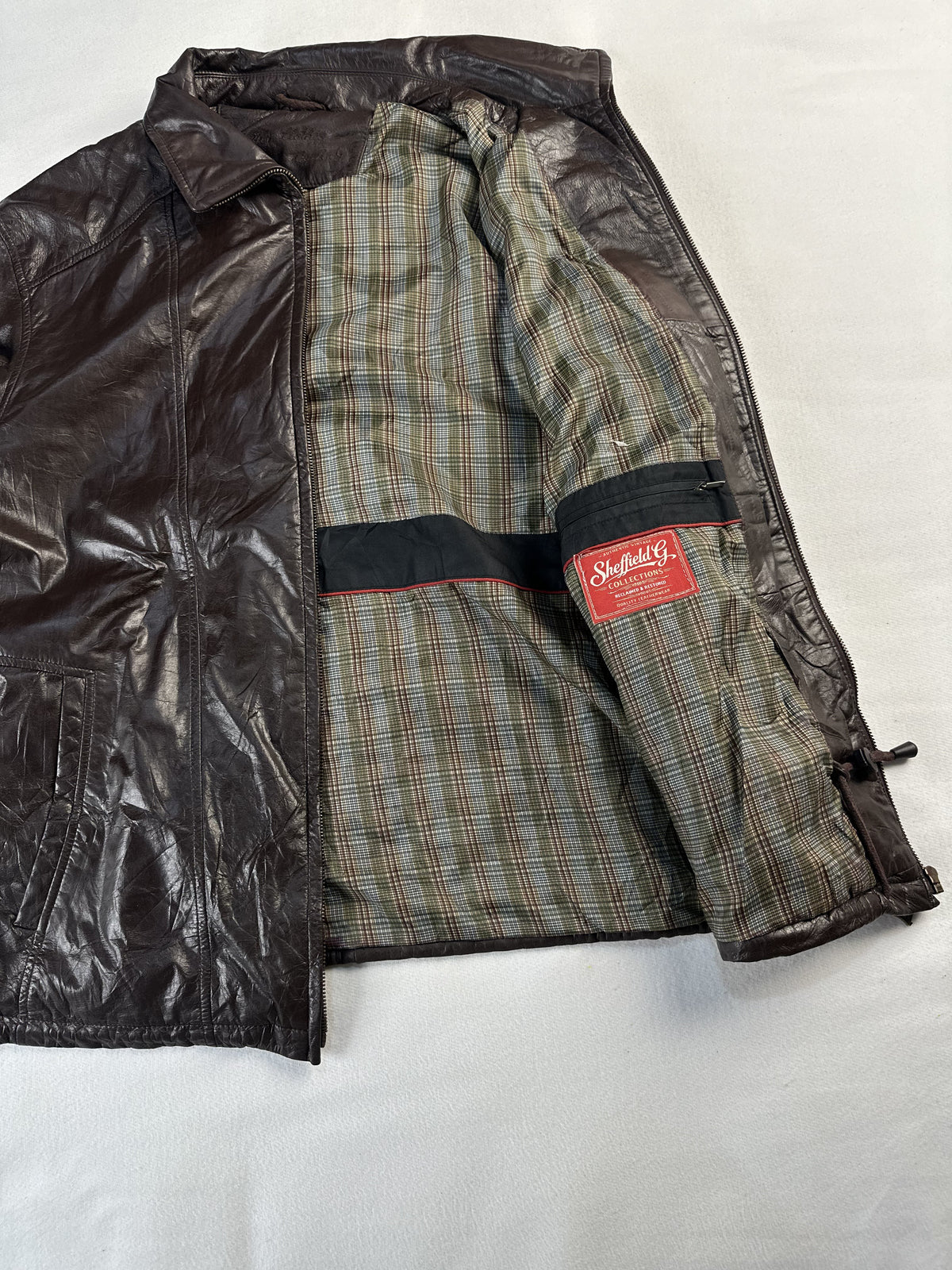 Green and tan check lining inside the brown jacket, held open to show the interior