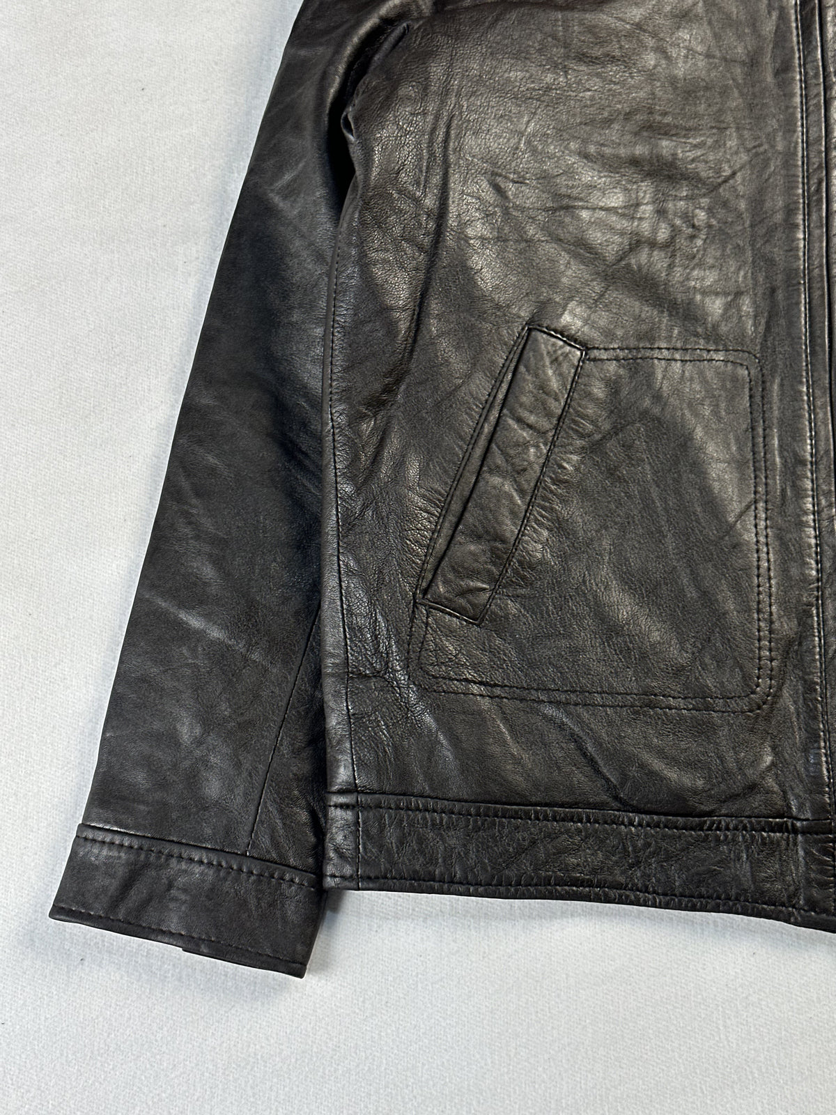Angled slash pocket, plain cuff and stitched hem at the lower left of the brown leather