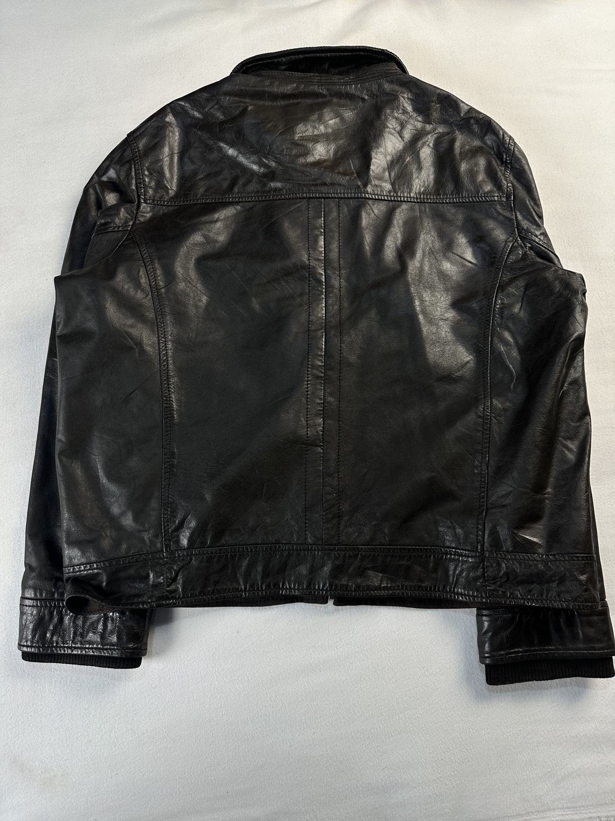 Back of the bomber laid flat, plain leather with a seamed yoke and a banded hem