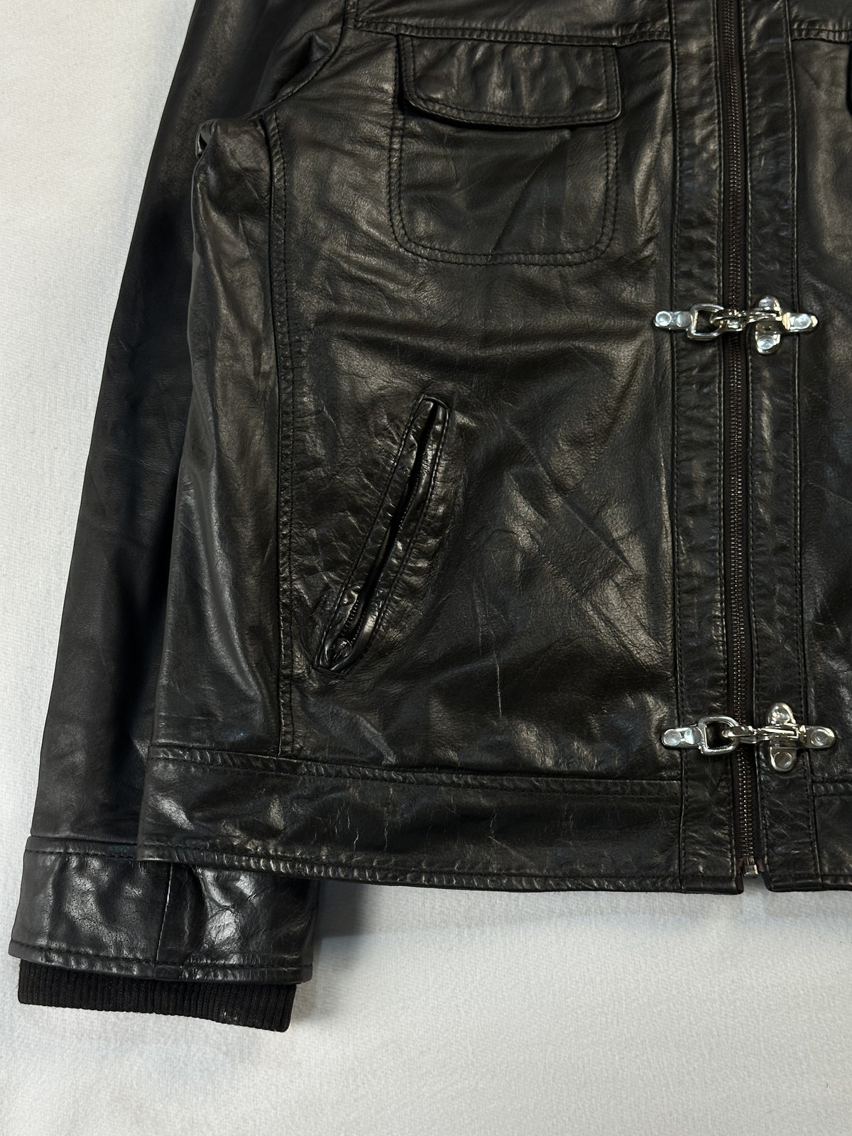 Detail of a slanted zip pocket, a clasp fastening and the knitted cuff at the hem