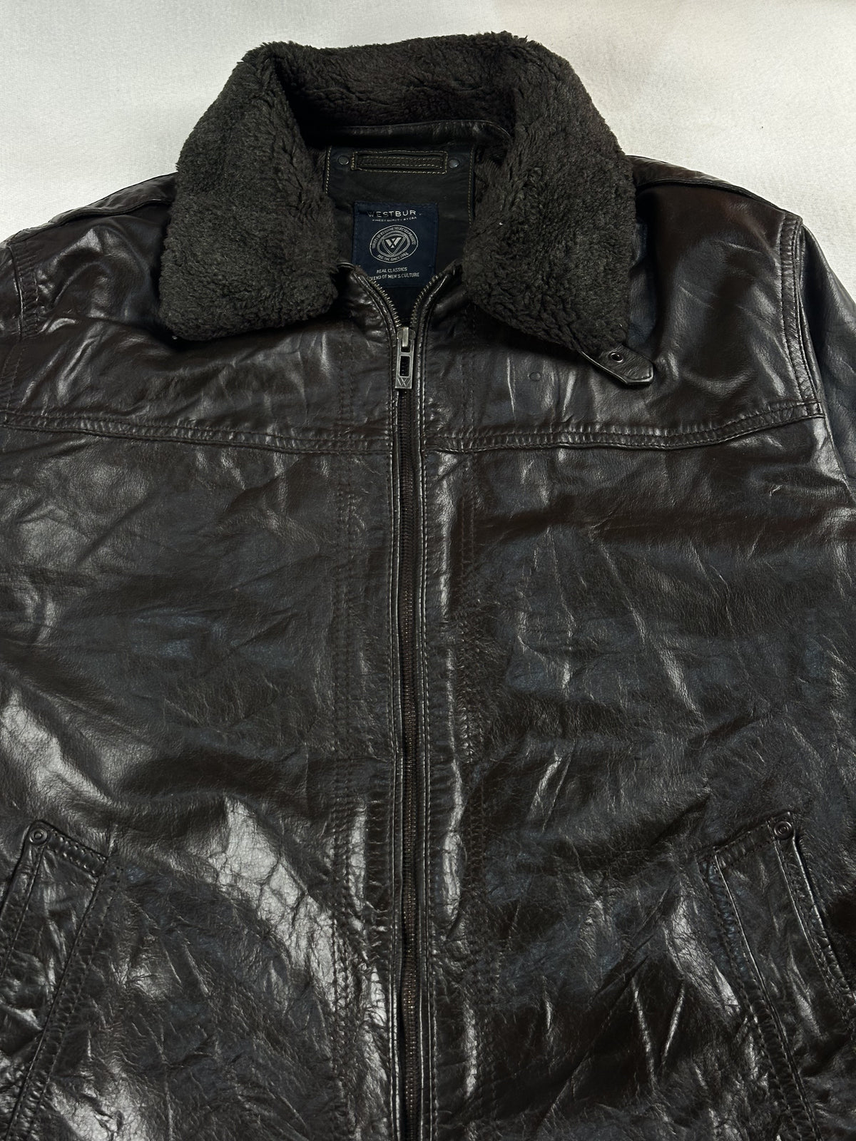Close view of the dark shearling collar and zip pull at the neck of the brown jacket