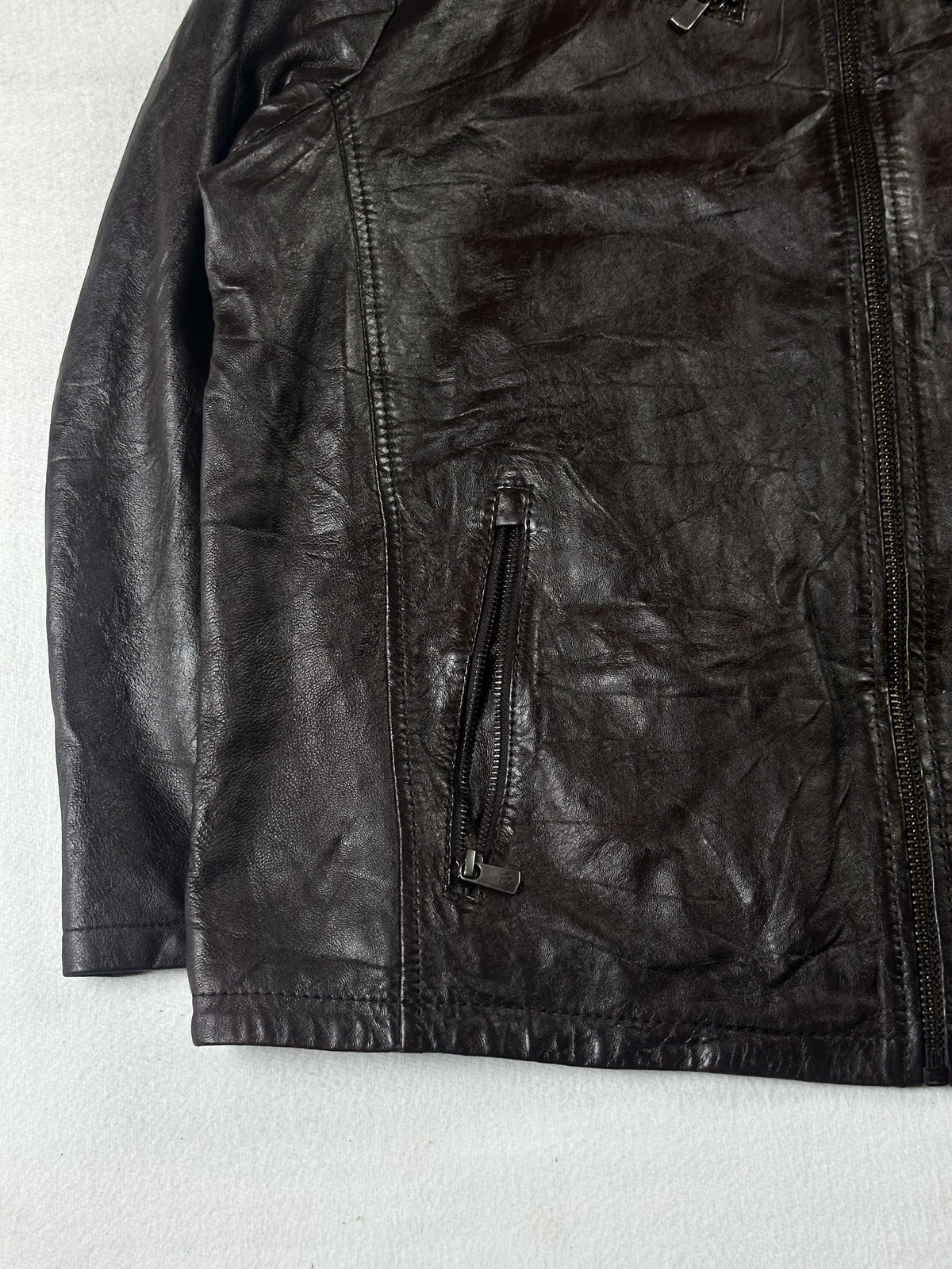 Angled view of a zipped hand pocket above the plain hem of the brown leather