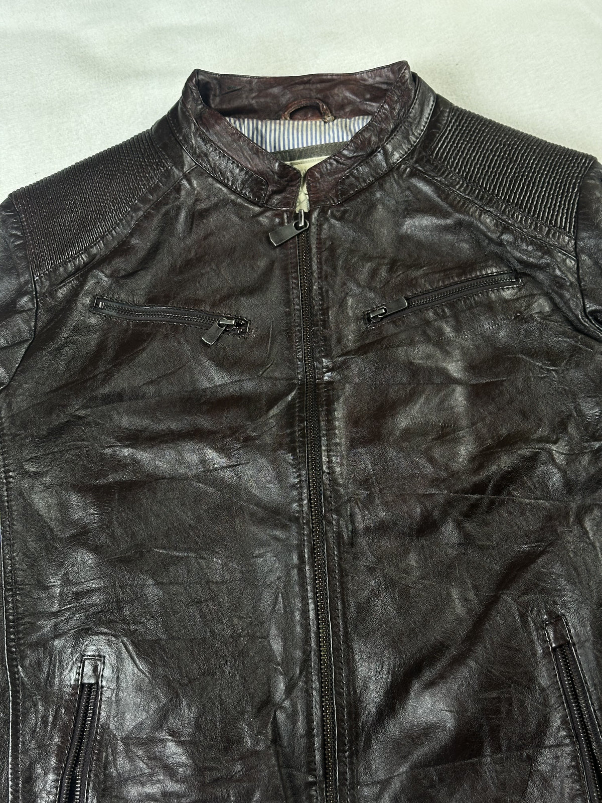 Close view of the band collar and twin zipped chest pockets on the brown jacket