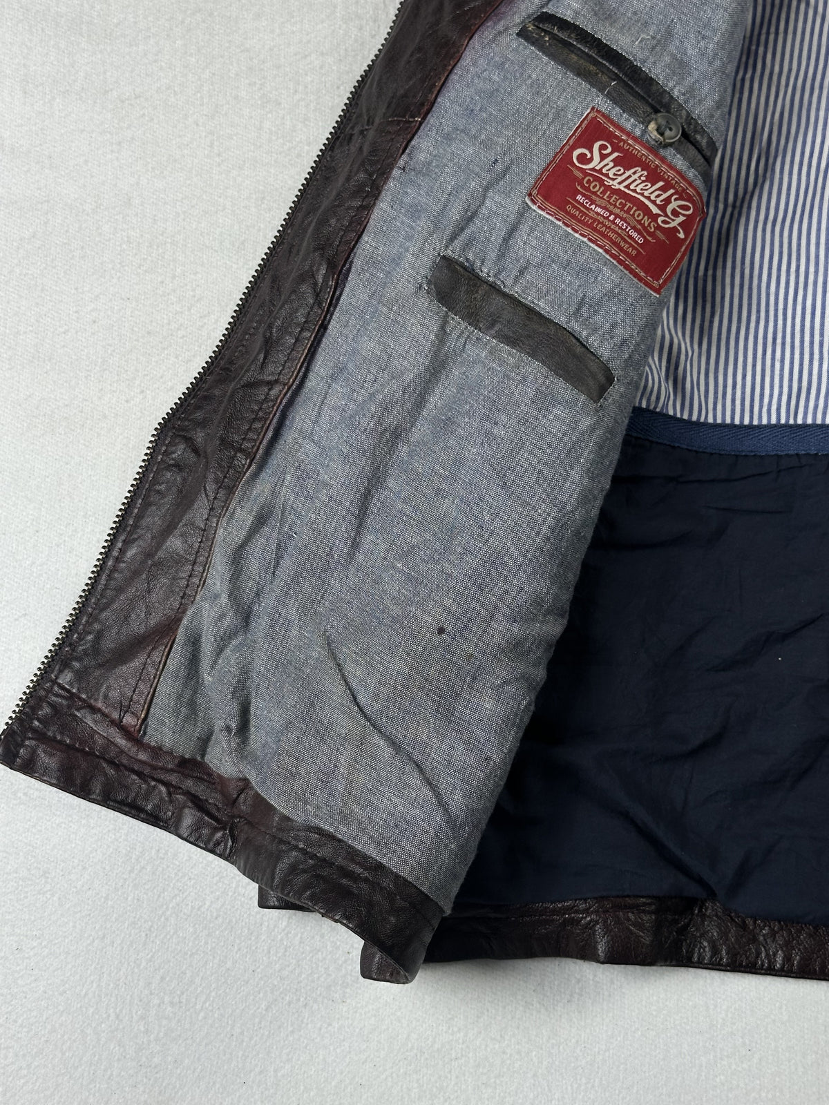 Blue and white striped lining beside a grey inner pocket in the open brown jacket