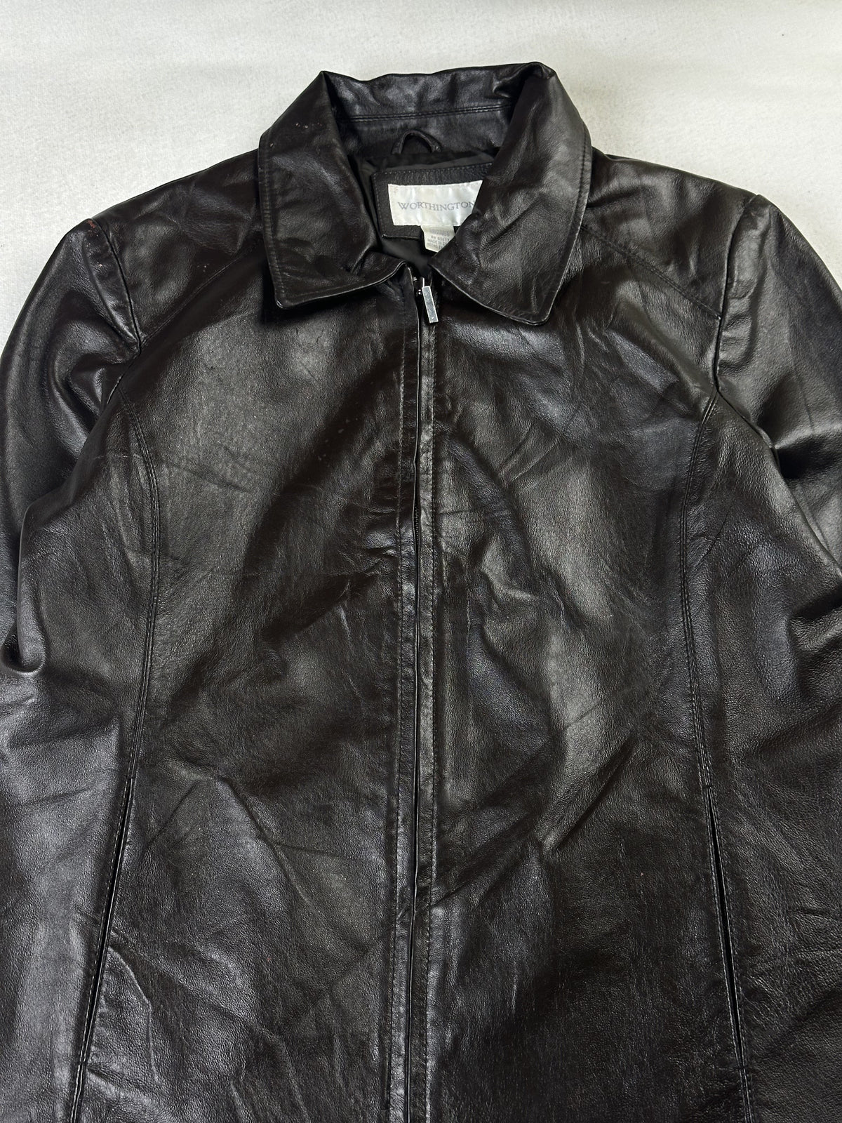 Close view of the point collar, neck label and zip pull on the brown leather jacket