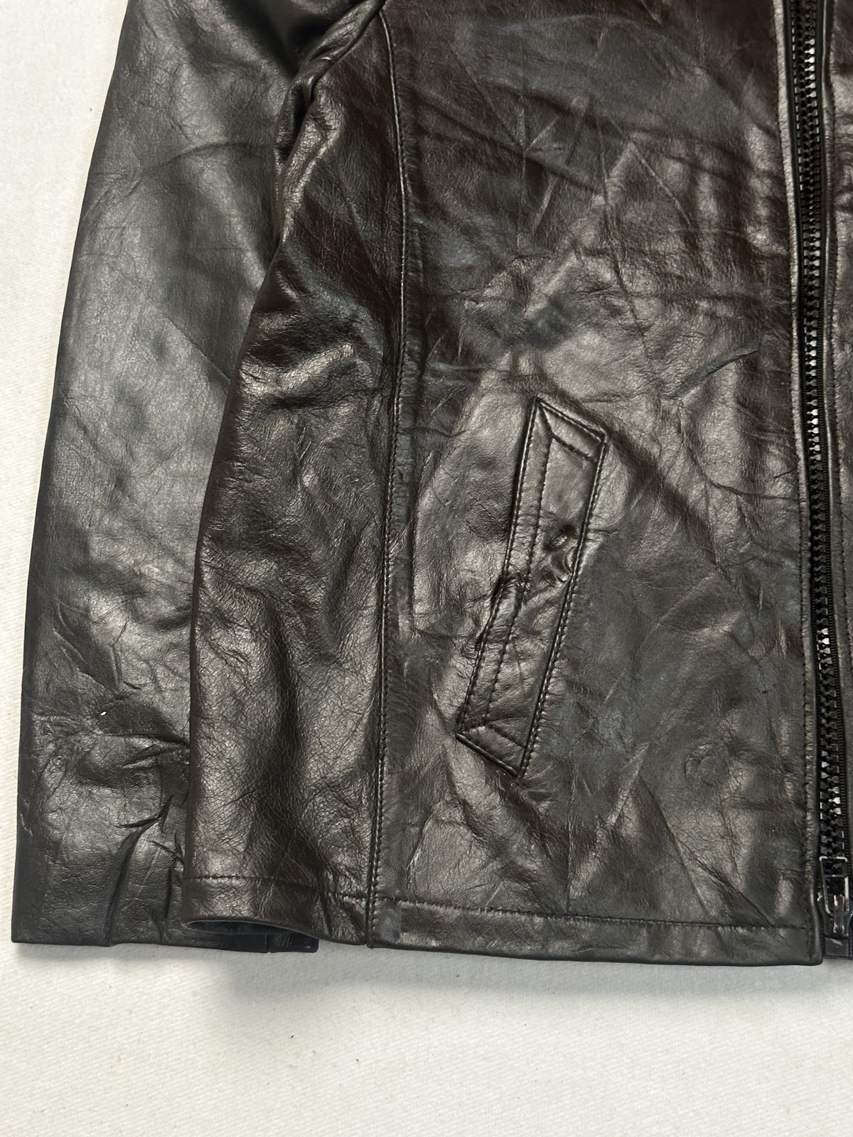 Angled view of a slanted welt pocket and the front zip on the brown leather