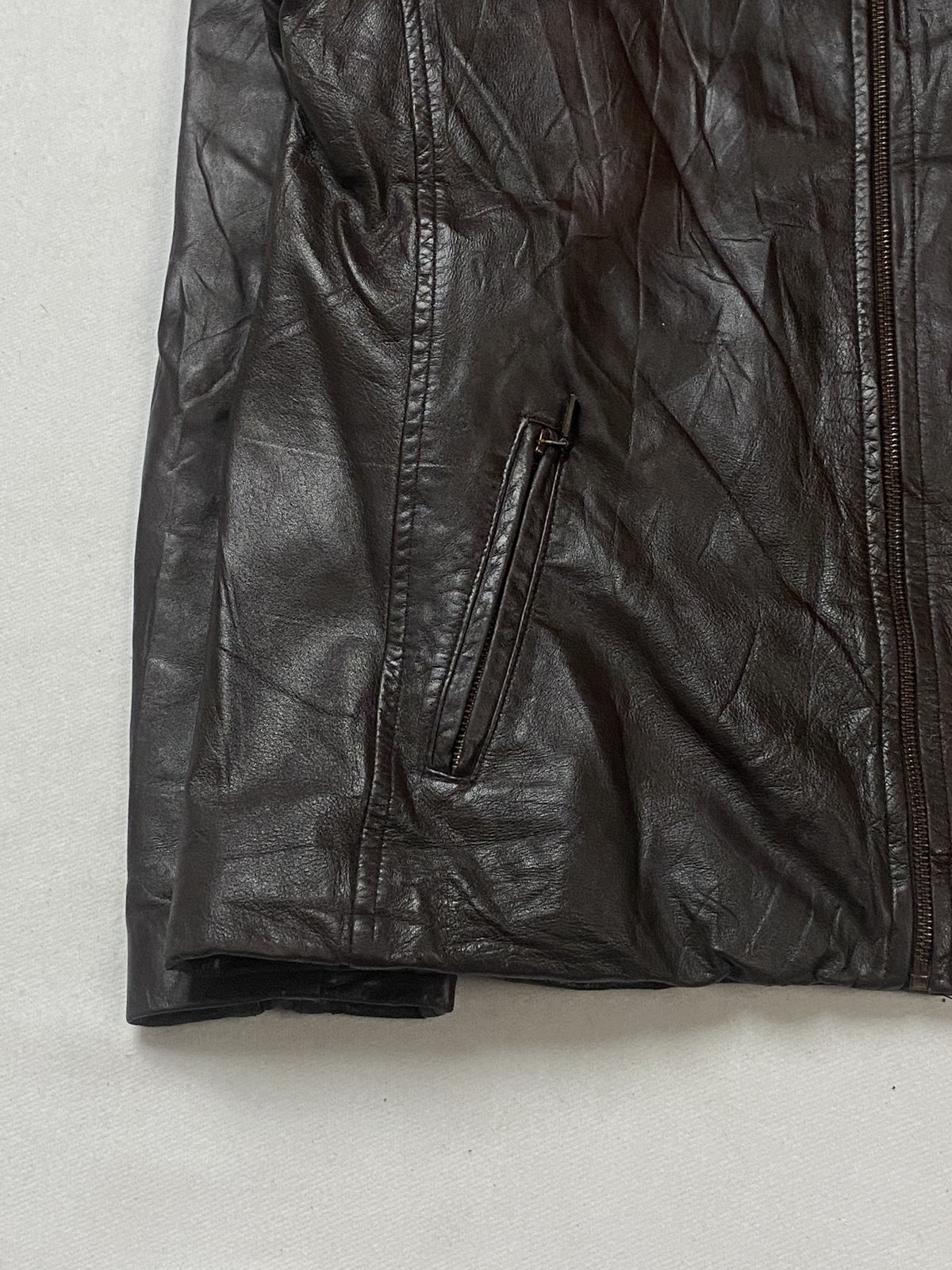 Slanted welt zip pocket and straight hem on the left front of the brown jacket