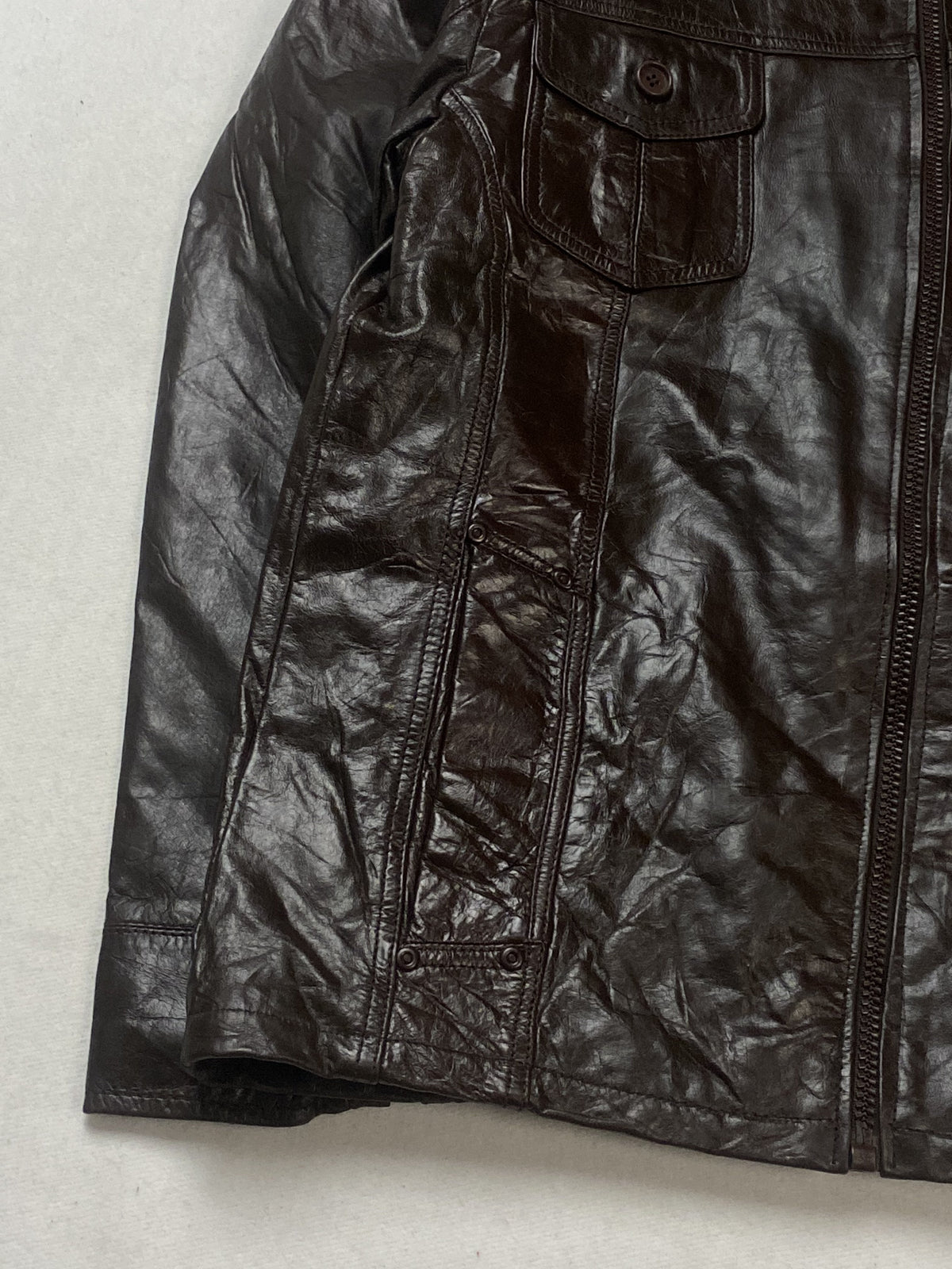Lower left front of the brown leather jacket with its stitched side panel and hem