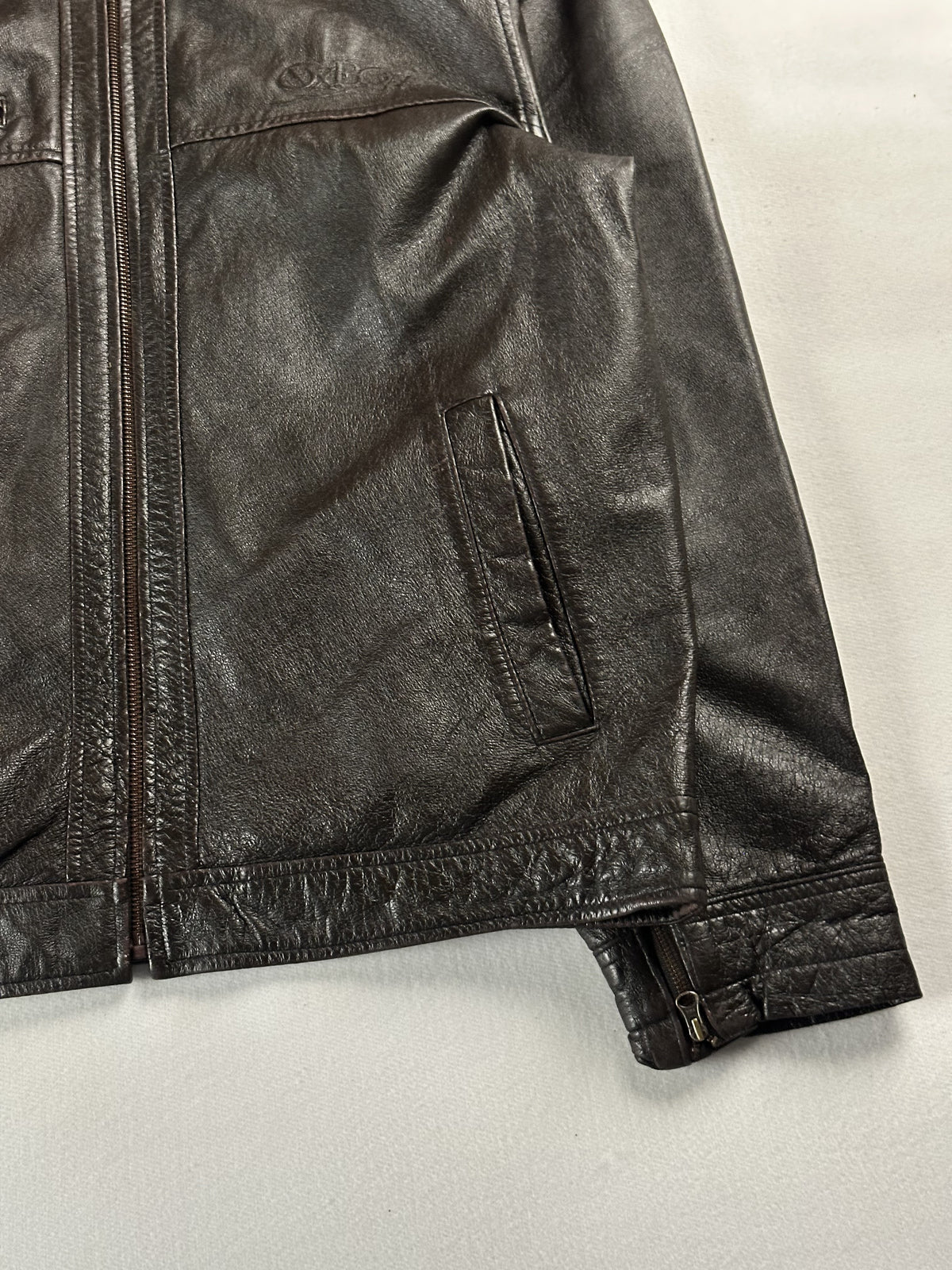 Close view of the centre zip meeting the hem band beside a zipped sleeve cuff