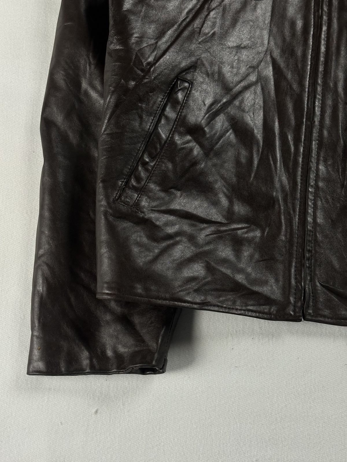 Angled welt pocket set into the lower left front of the brown leather jacket