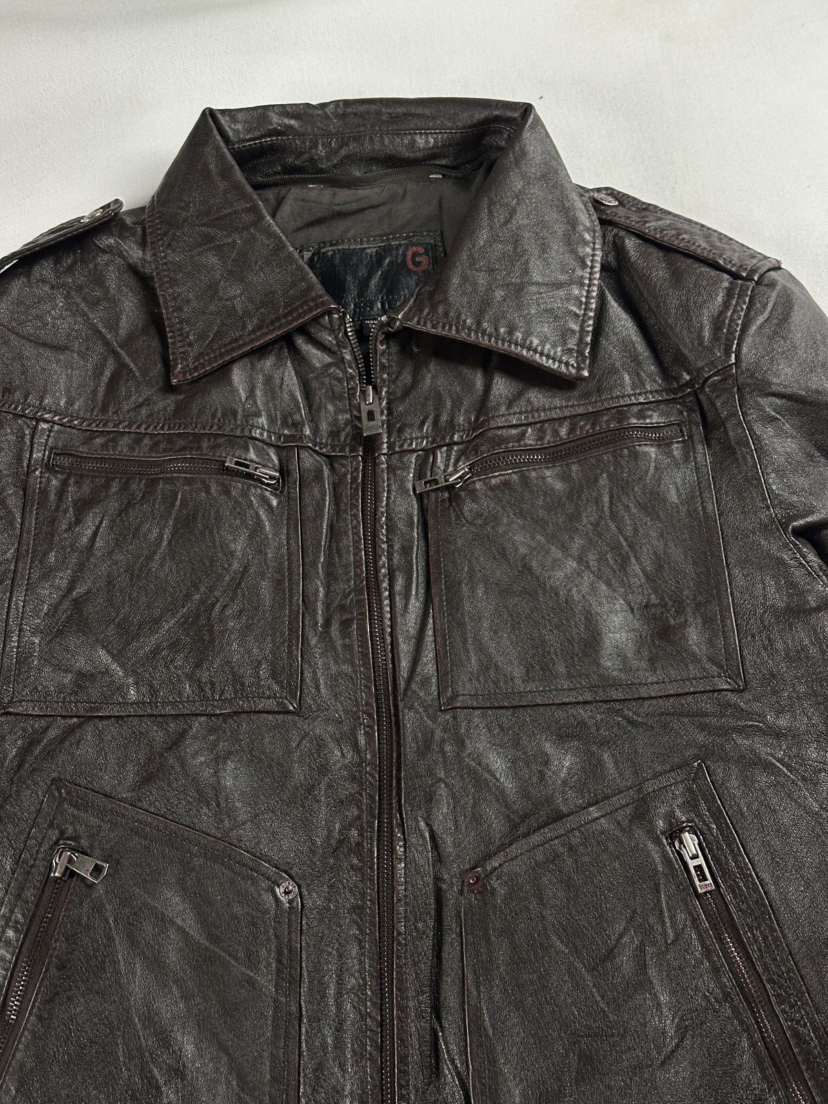Close view of the pointed collar, front zip and chest pockets on the brown leather