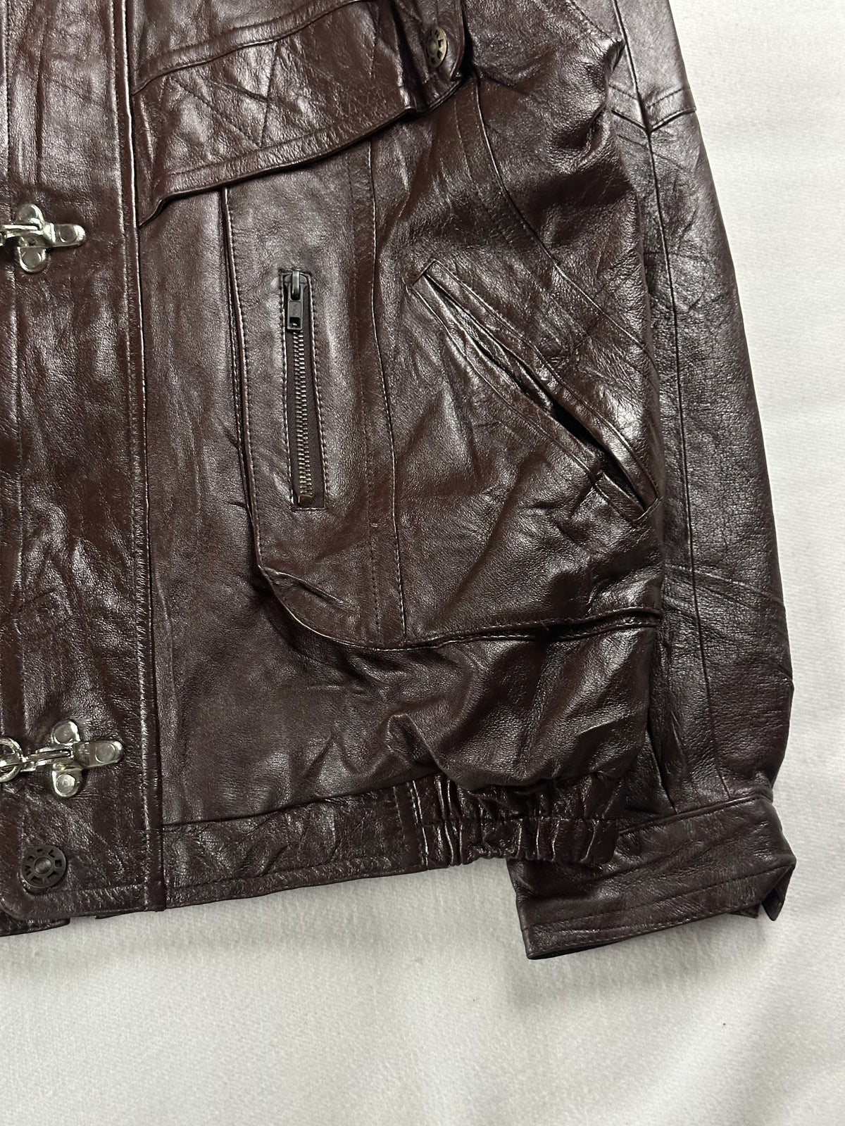 Flap pocket, slim zip pocket and cuff on the right side of the brown leather