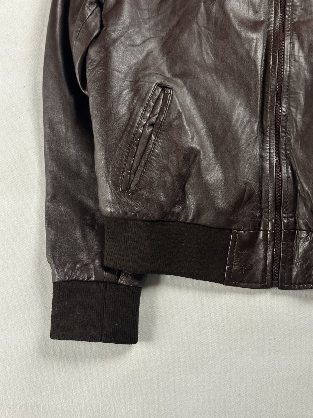 Slanted zip pocket at the left front, above the ribbed hem and cuff of the brown jacket