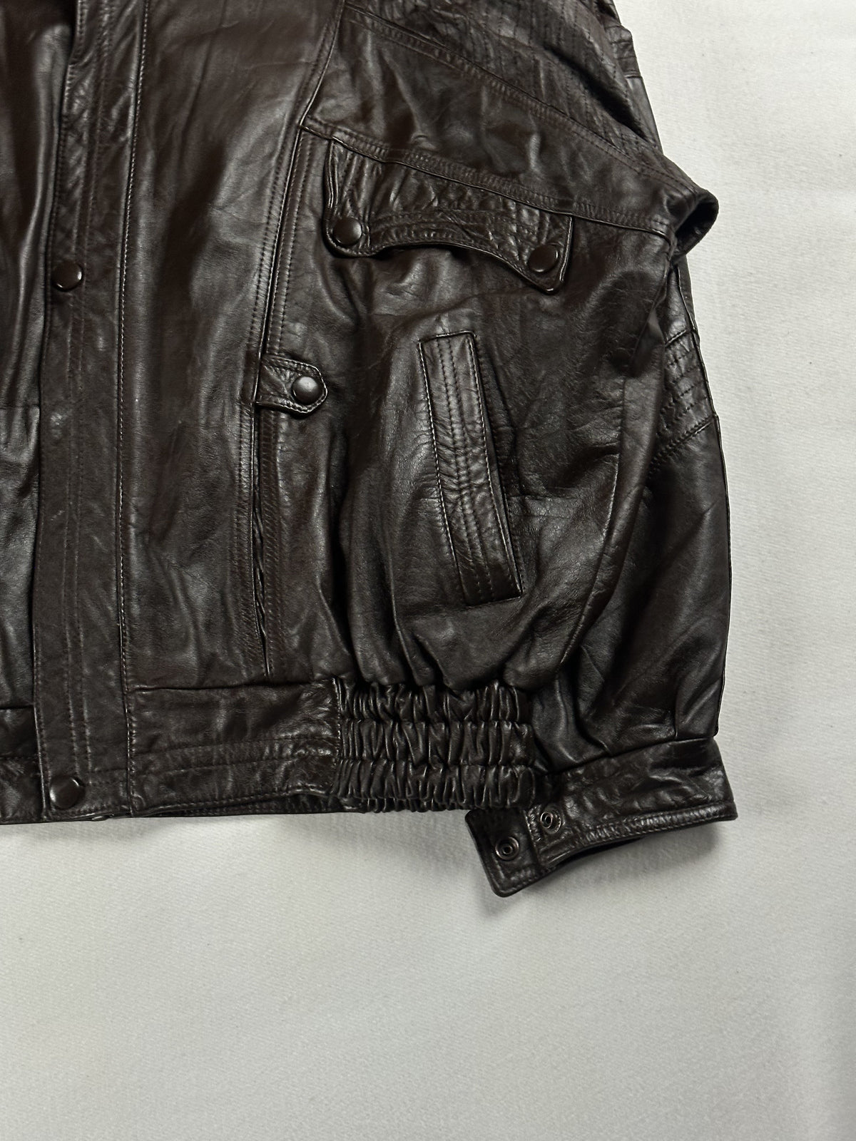 Close view of the popper-fastened pocket flap and buttoned cuff on the brown leather