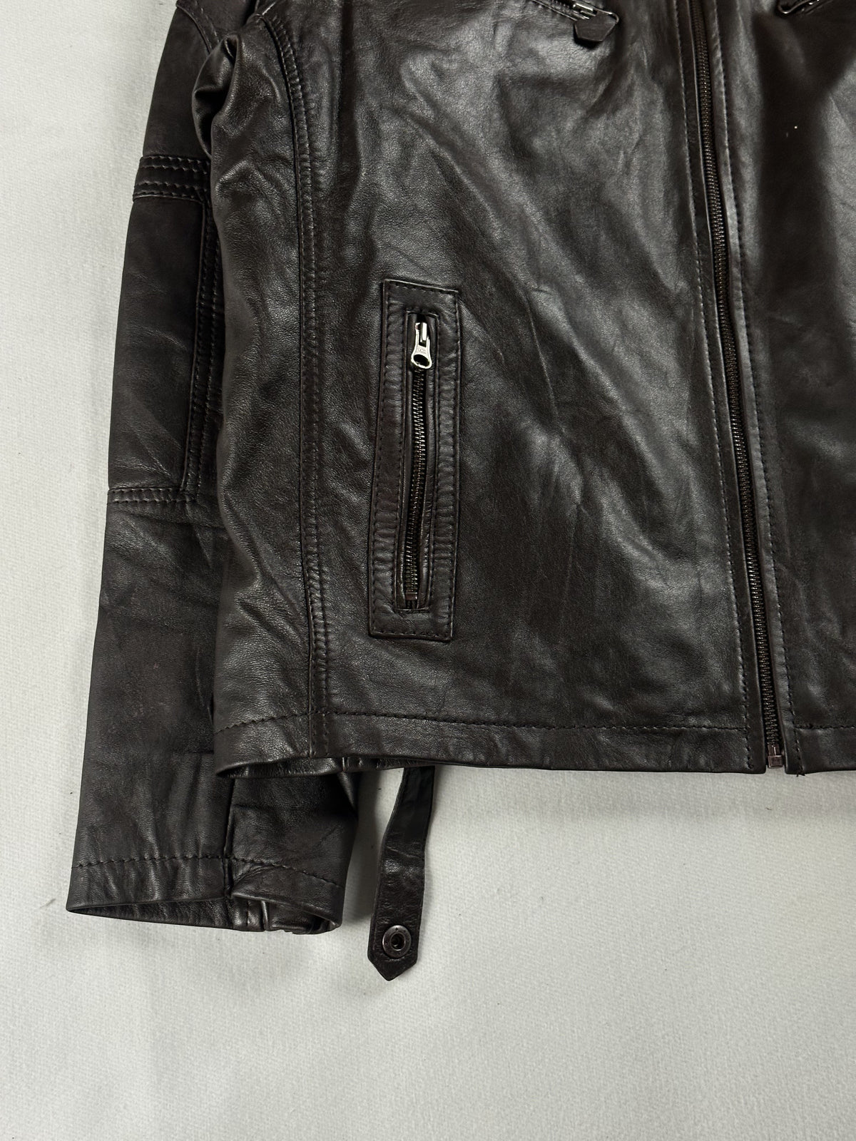 Detail of a zipped welt pocket above the buckled strap at the hem