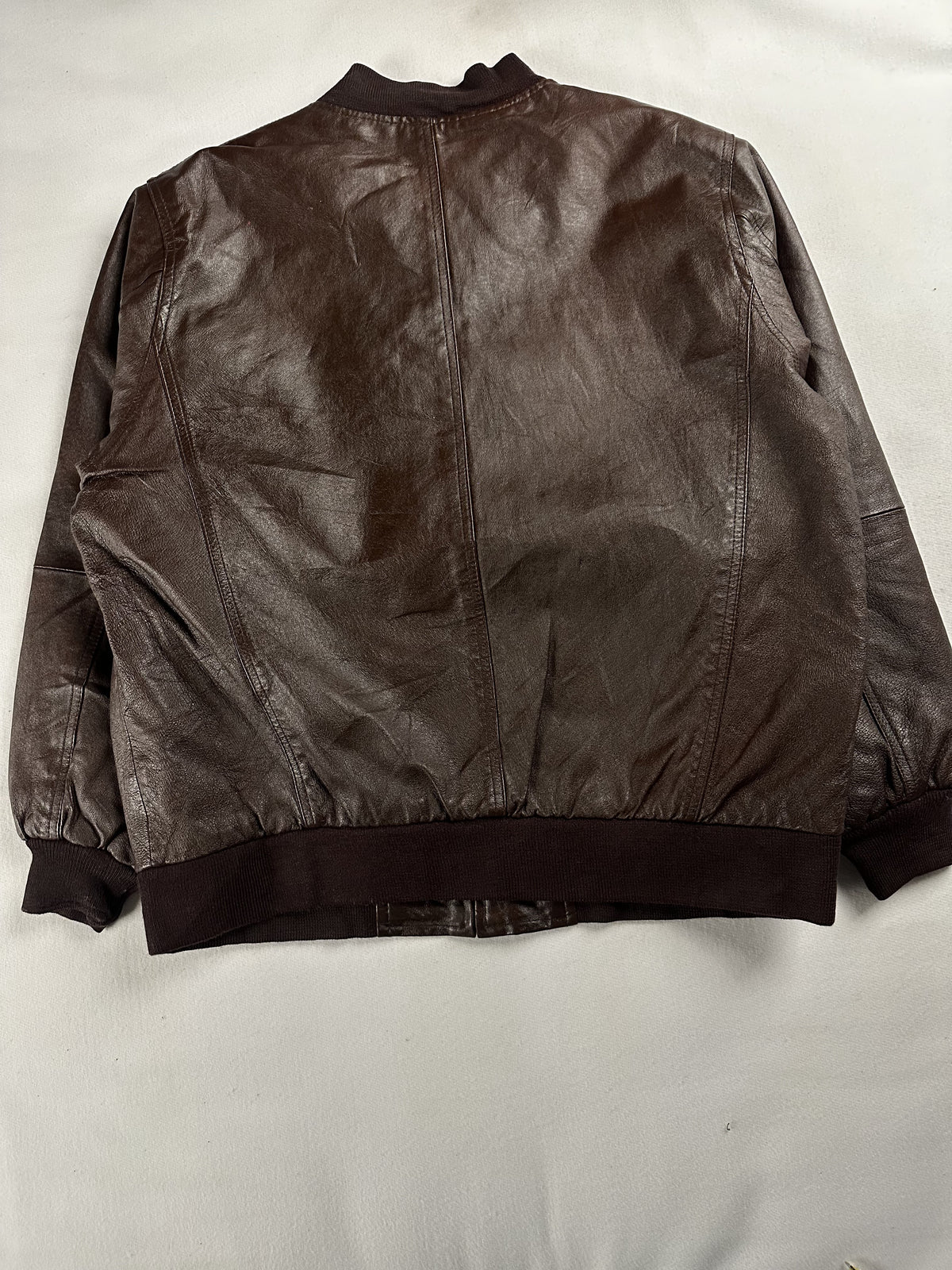 Back of the XL bomber laid flat, plain leather above a wide ribbed hem
