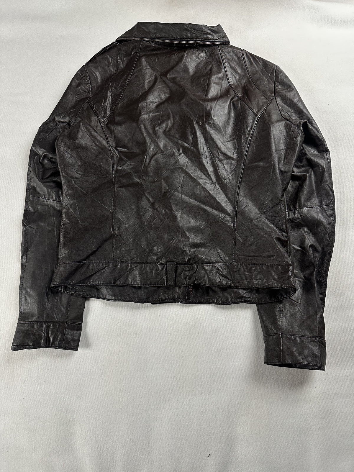 Back of the small biker jacket laid flat, plain leather with a belt strap at the waist