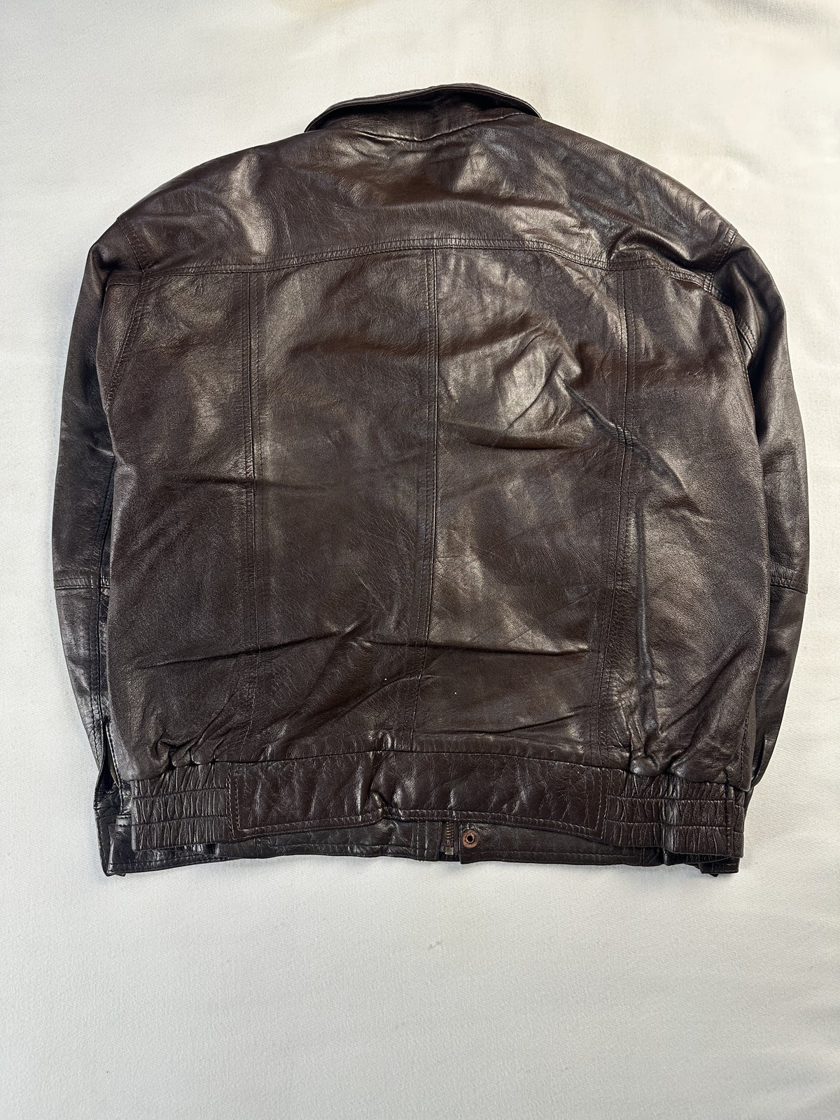 Rear view of the size L brown bomber laid flat with a buttoned tab at the ribbed waist