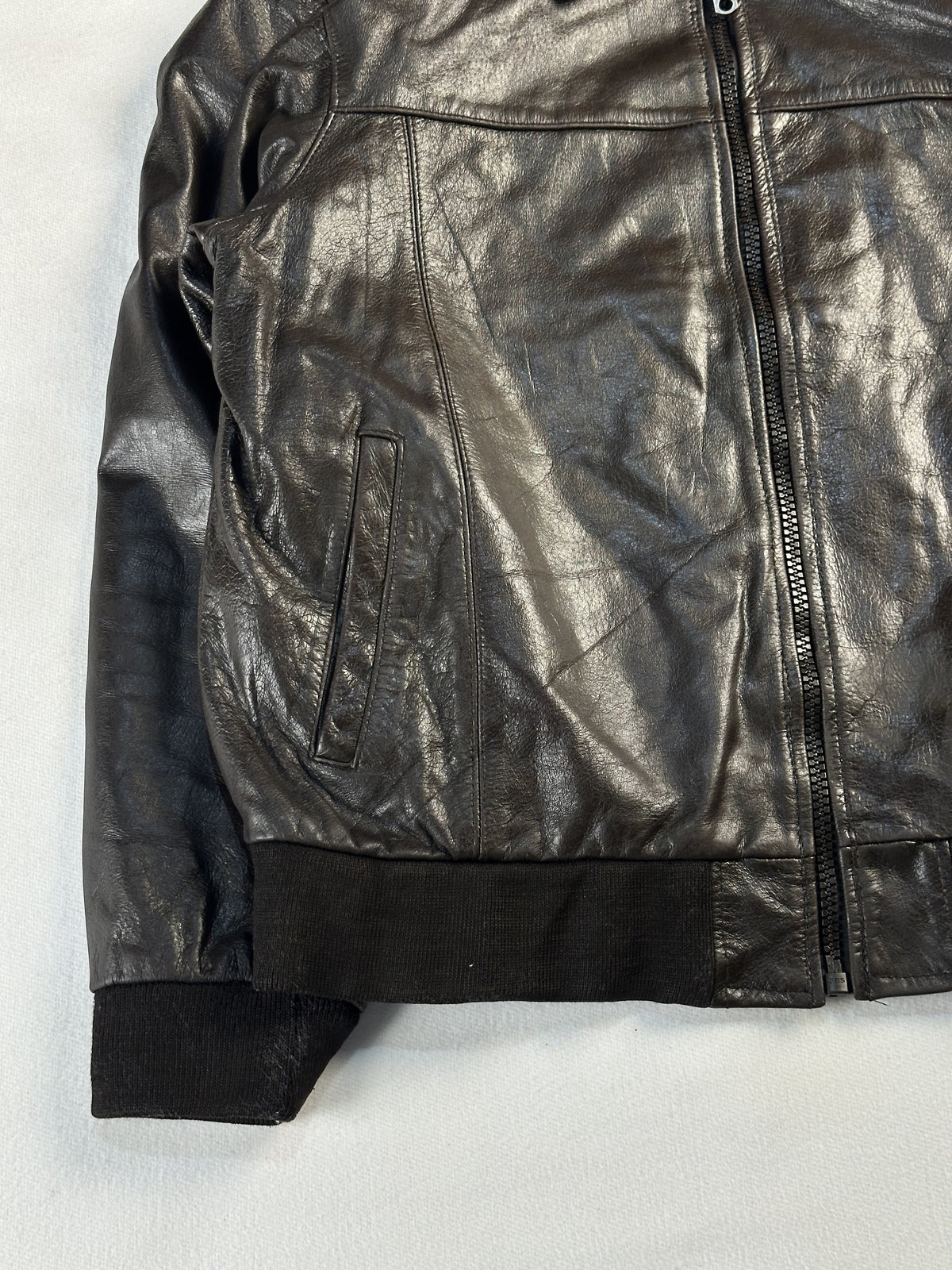 Left side welt pocket above the ribbed hem and cuff of the brown leather jacket