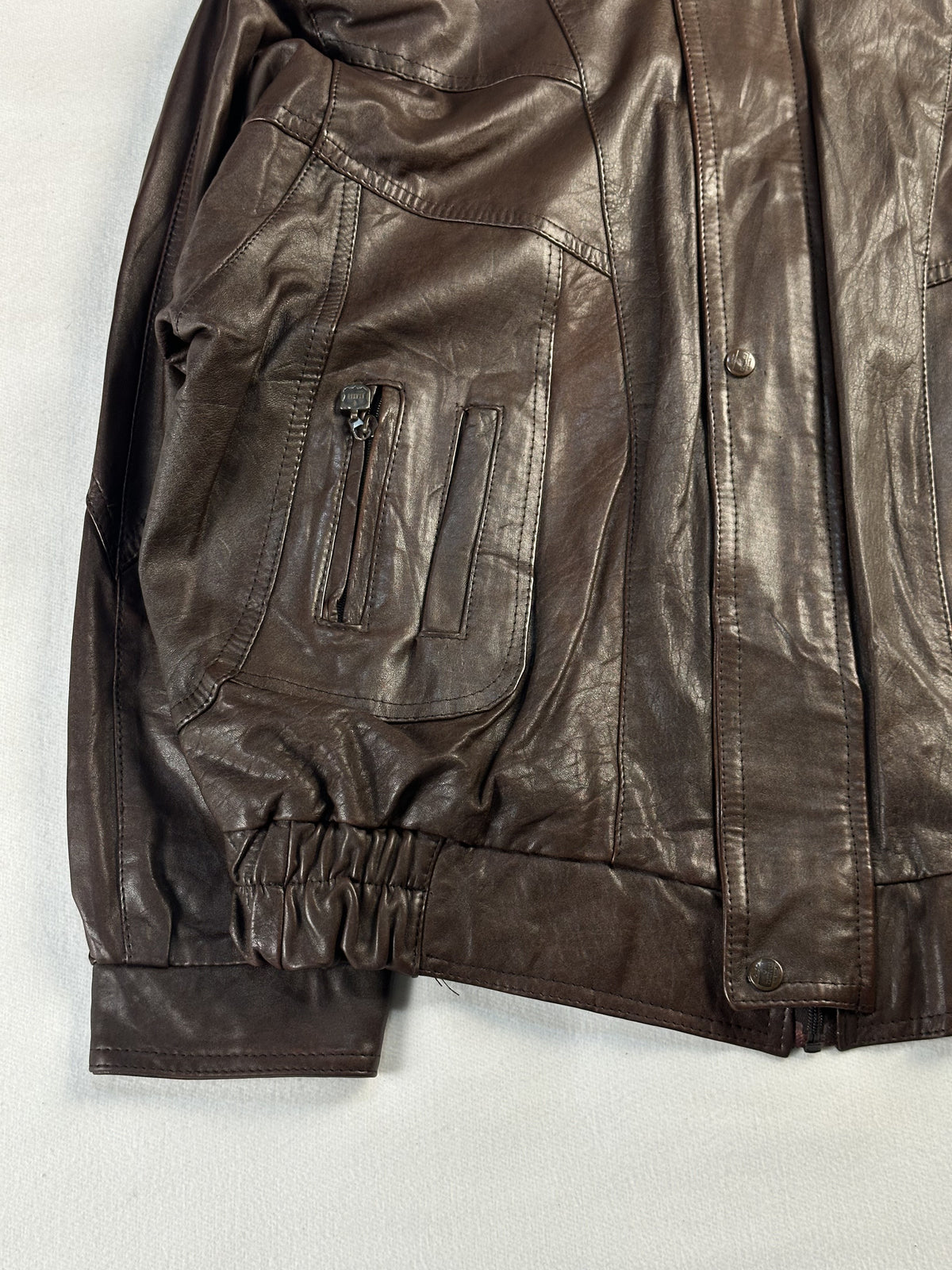Zipped patch pocket on the left front, above the gathered elastic waist of the brown jacket
