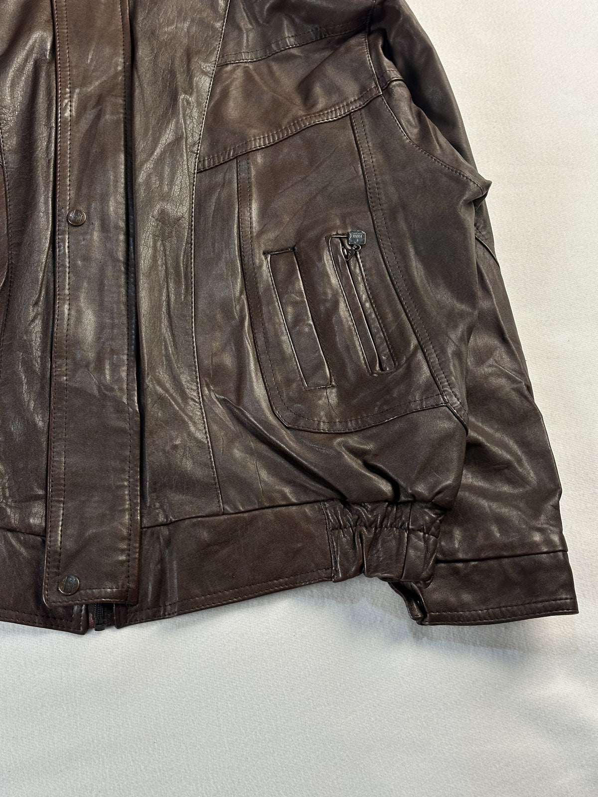 Right hand cargo pocket and press studs along the storm flap of the brown leather jacket