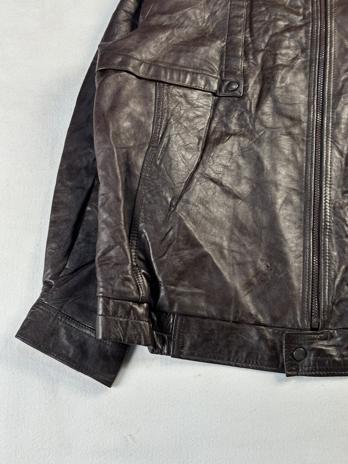 Detail of a flap pocket, front zip and the snap-tab waistband on the brown leather
