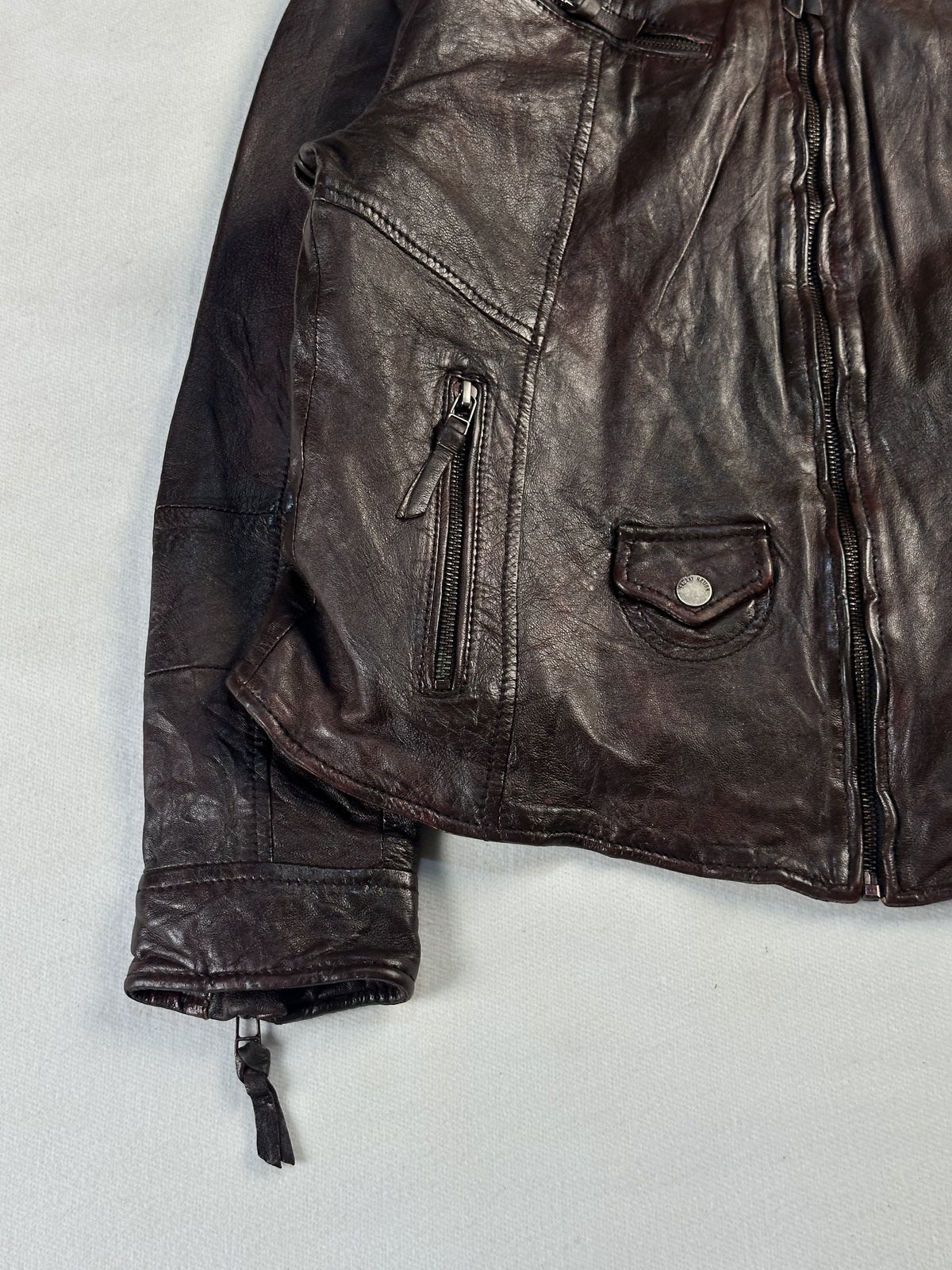 Zip pocket and studded flap pocket beside a cuff, with a drawstring cord hanging loose