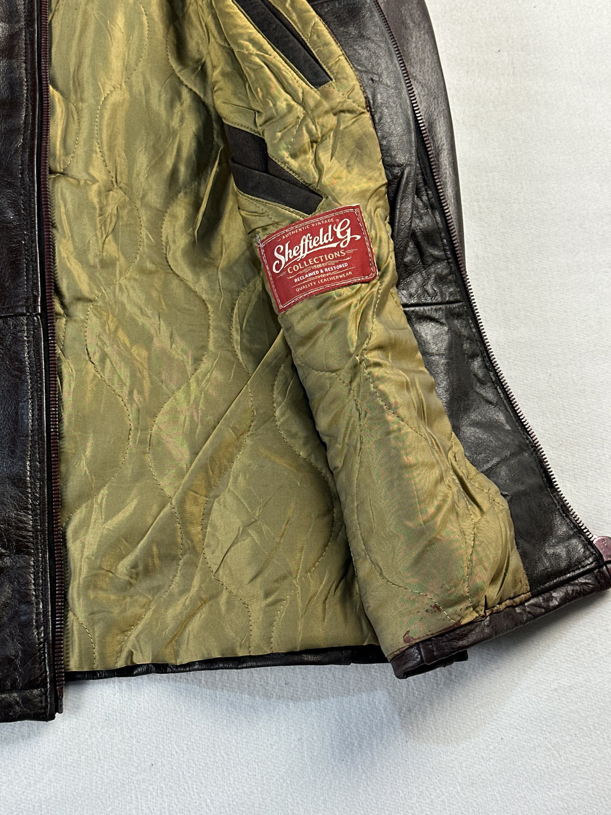 Olive quilted lining and red inner label inside the brown jacket, held open