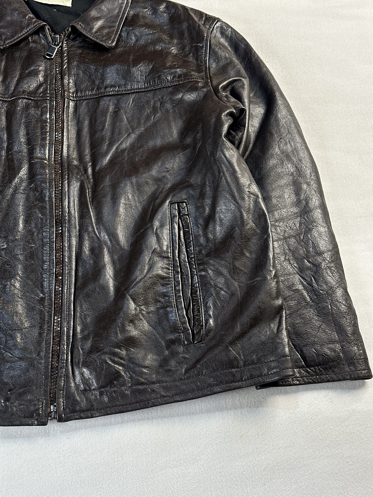 Angled detail of the centre zip and slanted zip pocket on the brown leather
