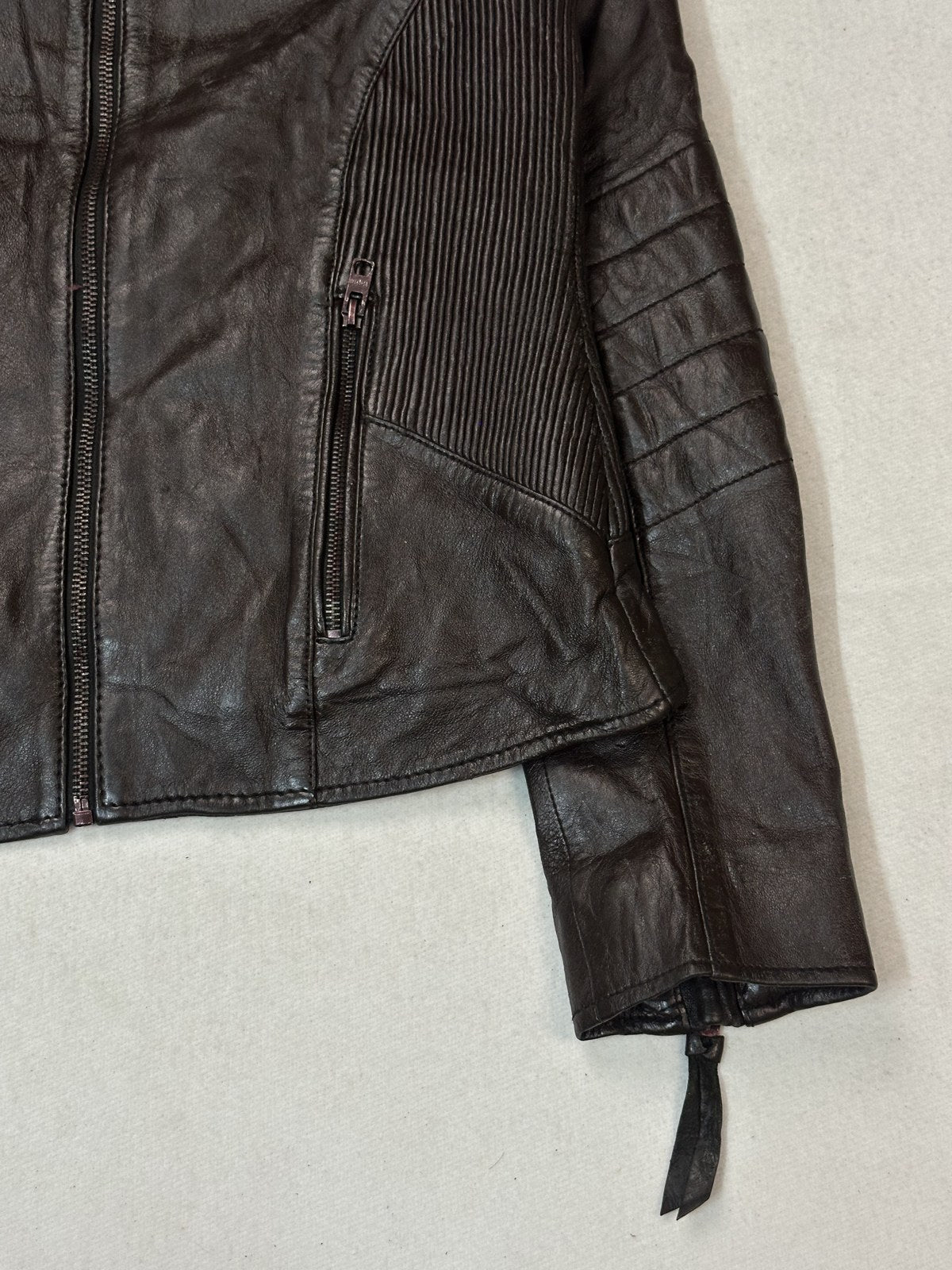 Close view of a ribbed side panel, zip pocket and cuff on the size S burgundy biker jacket