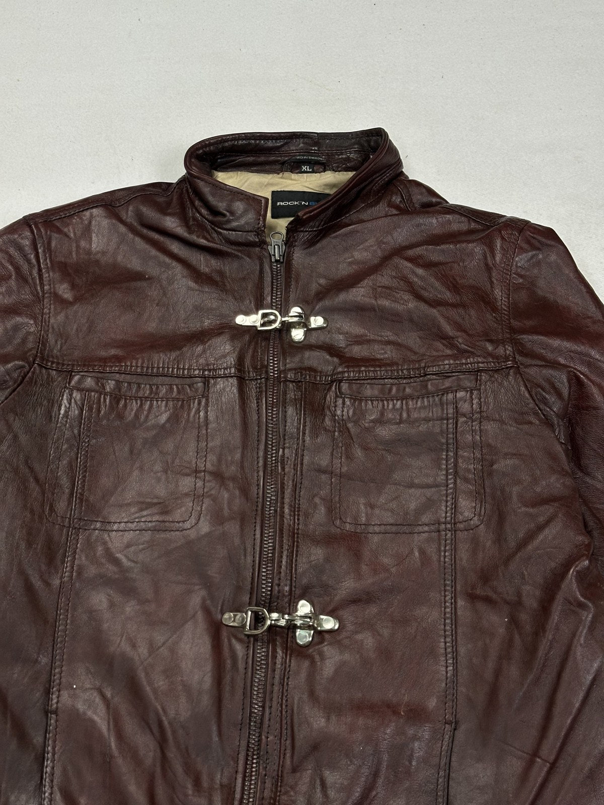 Close view of the stand collar and the top brass toggle clasp on the burgundy biker jacket