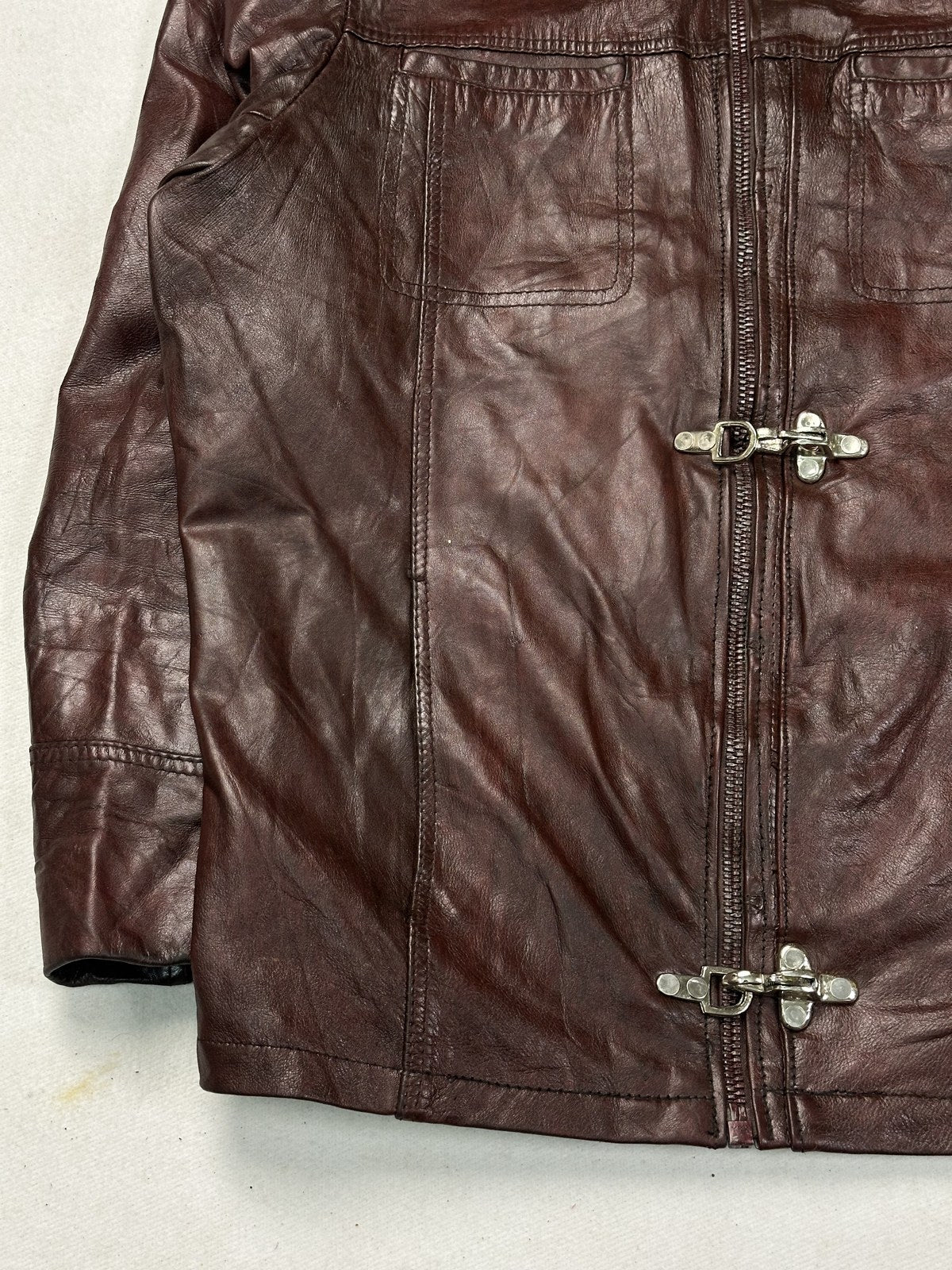 Detail of a brass toggle clasp against the grain of the burgundy leather