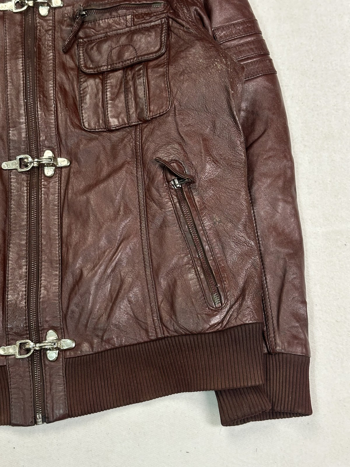 Detail of the worn brass clasp plate on the burgundy leather biker jacket